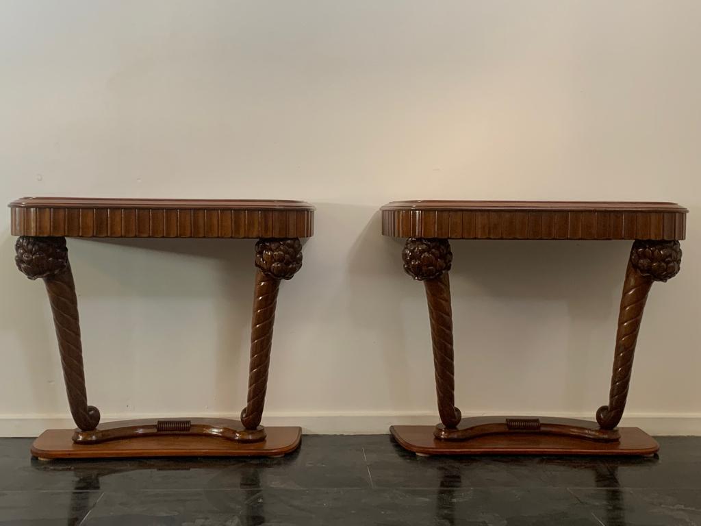 Beautiful and important pair of Art Deco consoles. Two finely carved pilasters with fruit finials start from the cherrywood base and support an undulating moulding that ends in a carved and threaded profile to accommodate the top. All in walnut, the