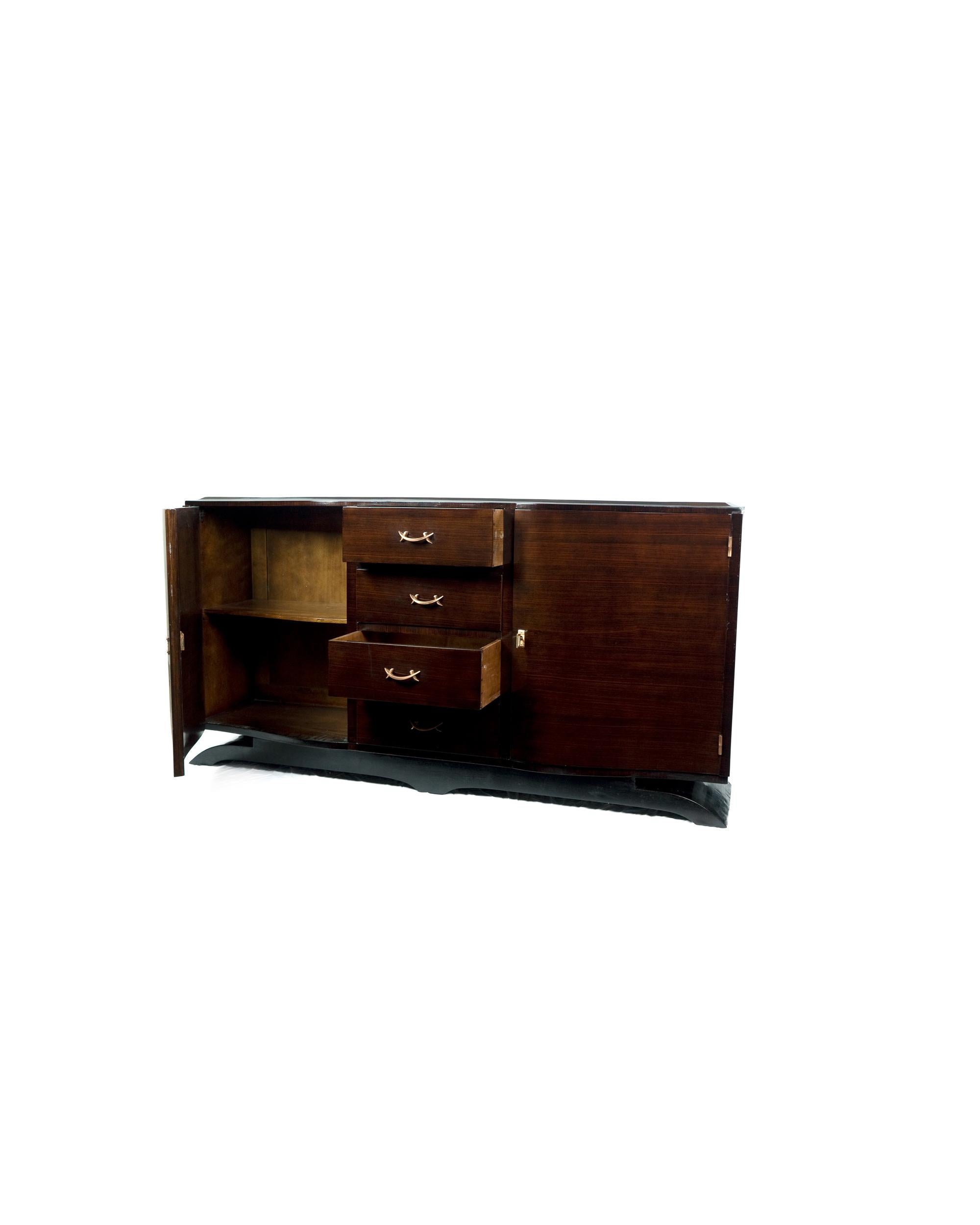 Cet impressionnant buffet Art déco du 20e siècle a une largeur de 200 cm et des ferrures plaquées de cuivre.
Il conserve des lignes de style symétriques et épurées dans une approche mid-century, soulignées par une base moustache exquise.

Une