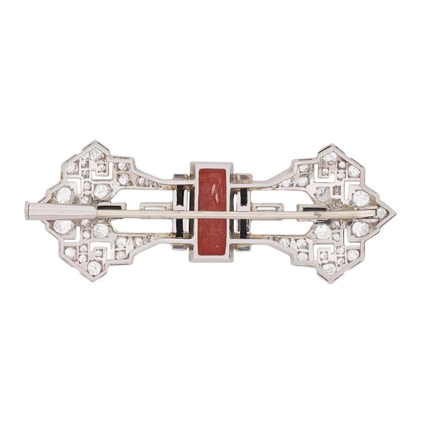 Dating from the 1920s, a stunning Art Deco period brooch set in platinum with a combination of coral, onyx, and baguette and old cut diamonds.

Chic and sophisticated, this striking piece is composed of strong geometric elements, juxtaposed with a