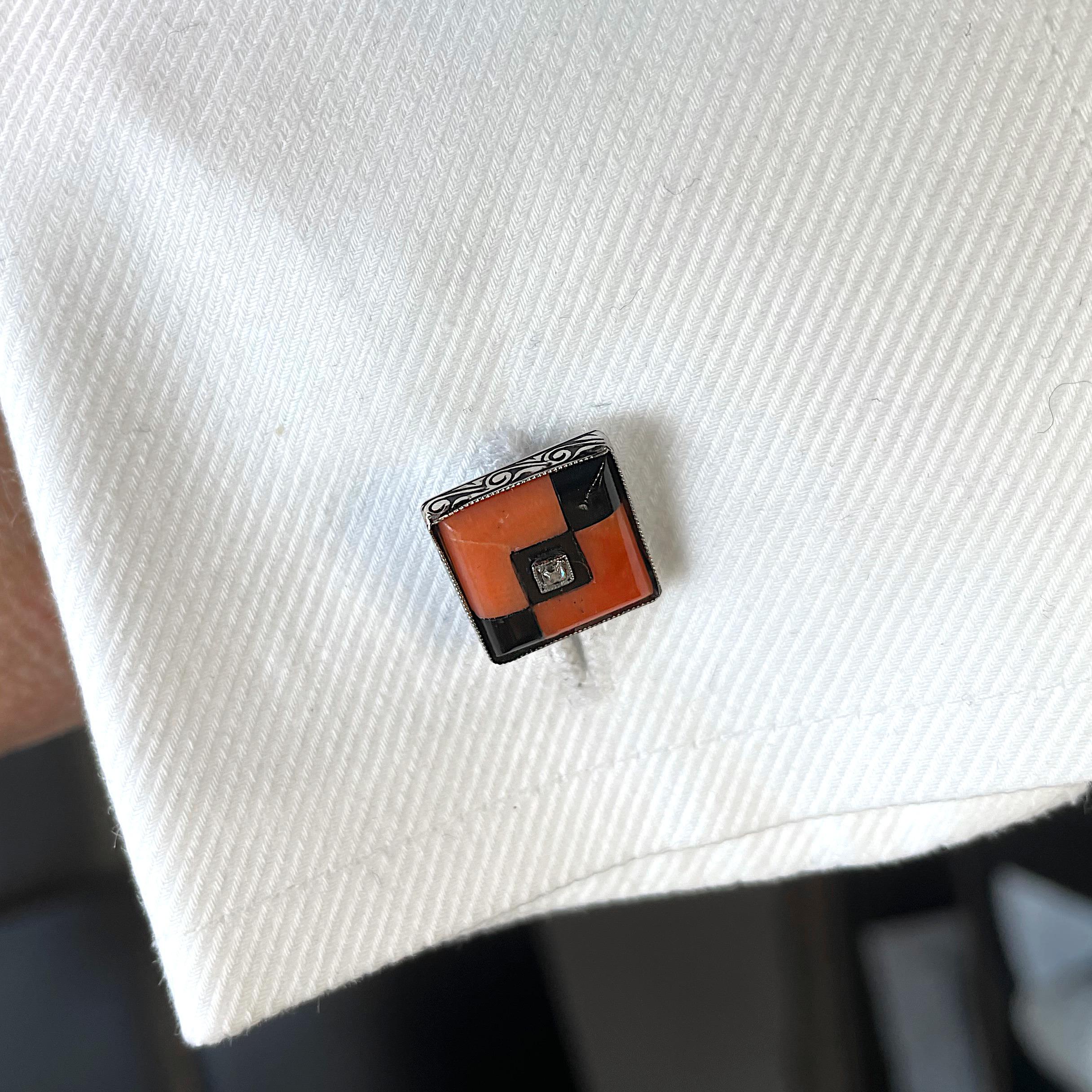 A pair of Art Deco, coral, black onyx and diamond cufflinks, with a diamond set in the centre of three, diagonally set, black onyx squares in a square geometric design, with coral right angles, mounted in platinum, with scrolling engraved sides, on