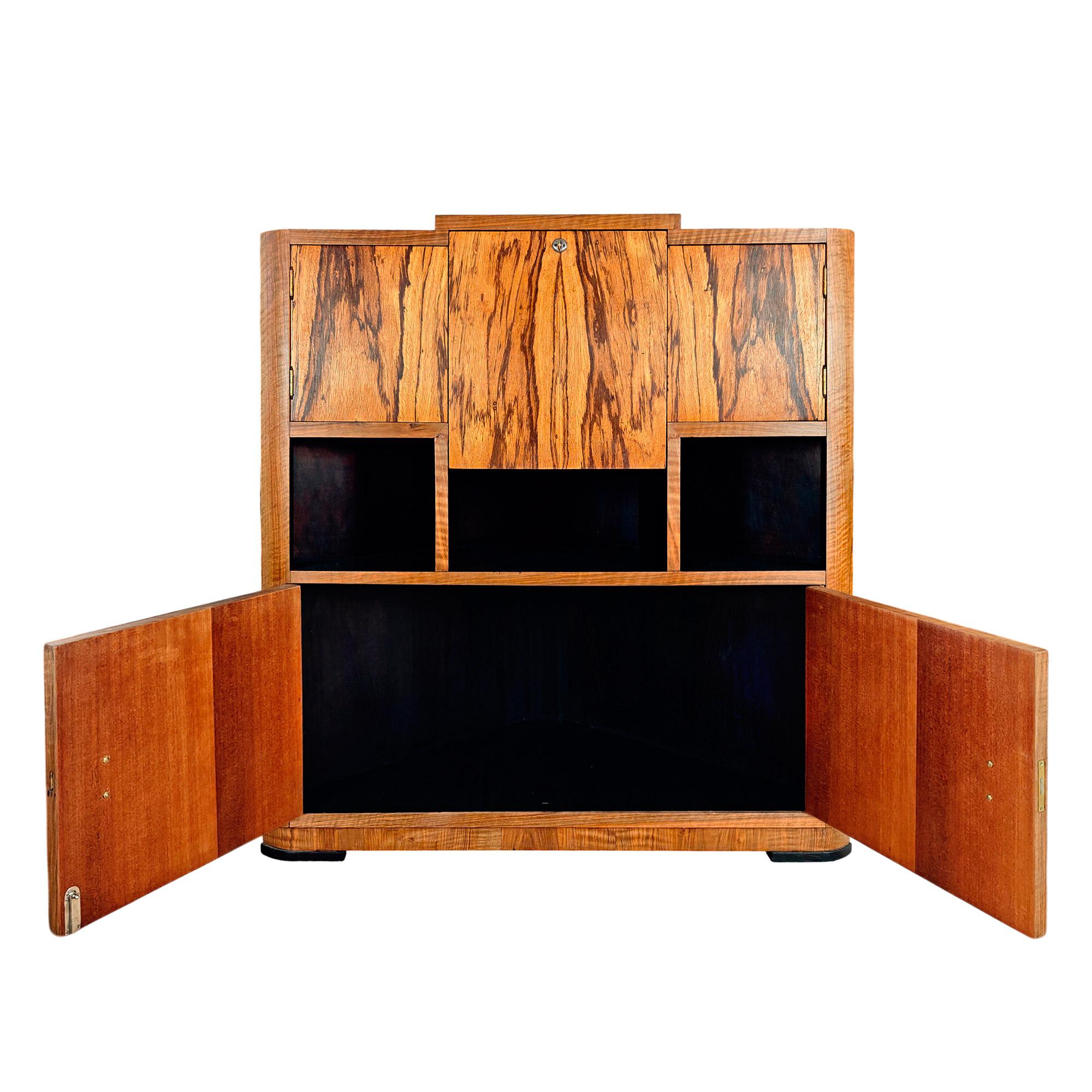 Meuble bar d'angle Art Déco en bois massif plaqué de noyer et de zebrano pour les portes, qui s'ouvrent (deux portes latérales et une porte à abattant) sur un intérieur garni de miroirs, de verre opalin noir et d'un plafonnier, de trois niches