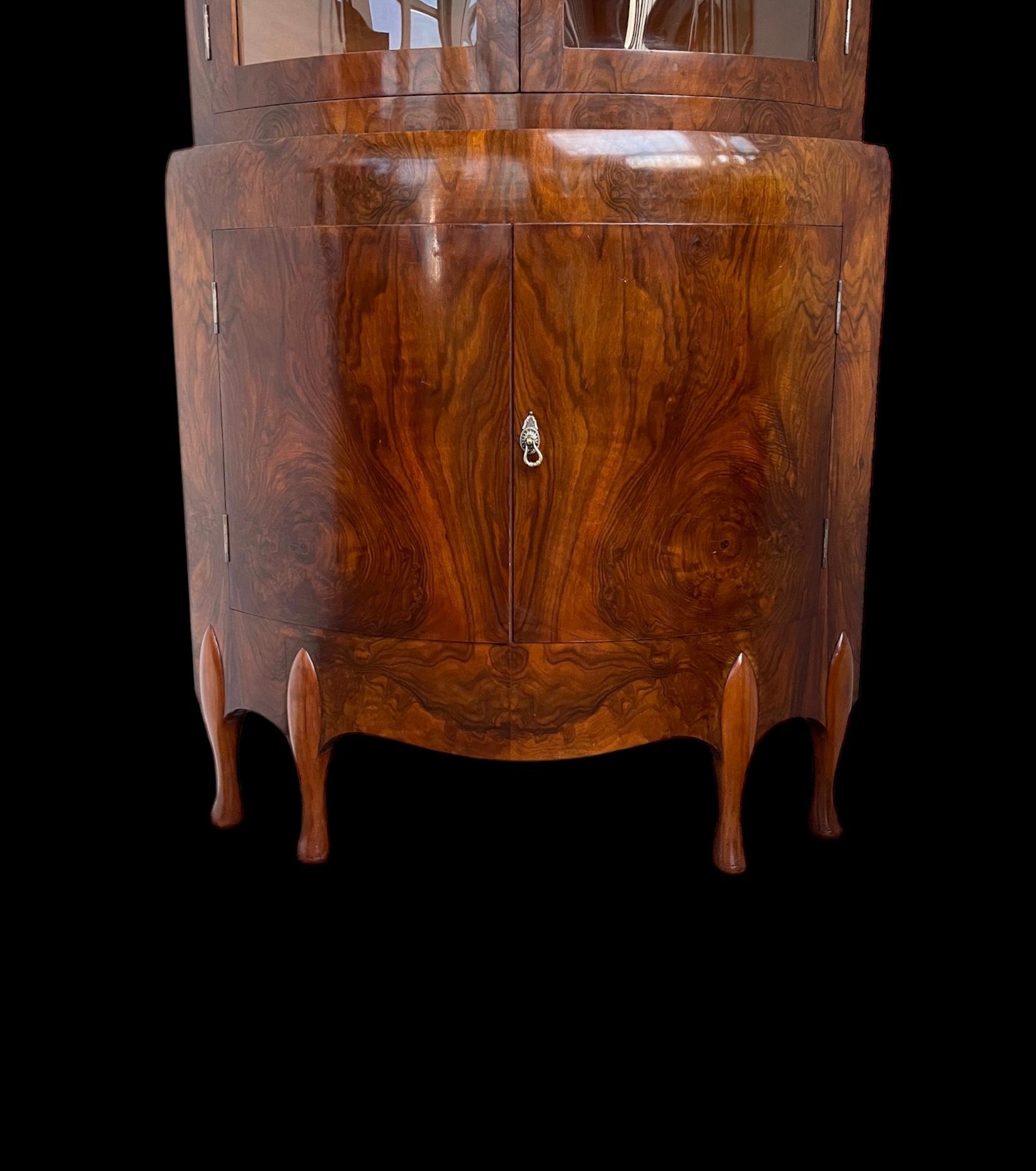 A fine Art Deco Maurice Adams corner display cabinet from the ‘Grosvenor’ range.  Circa.1925. 
Made in highly figured polished walnut, with three shelves to the top section, with two curved glass doors and it’s original working lock, key and two