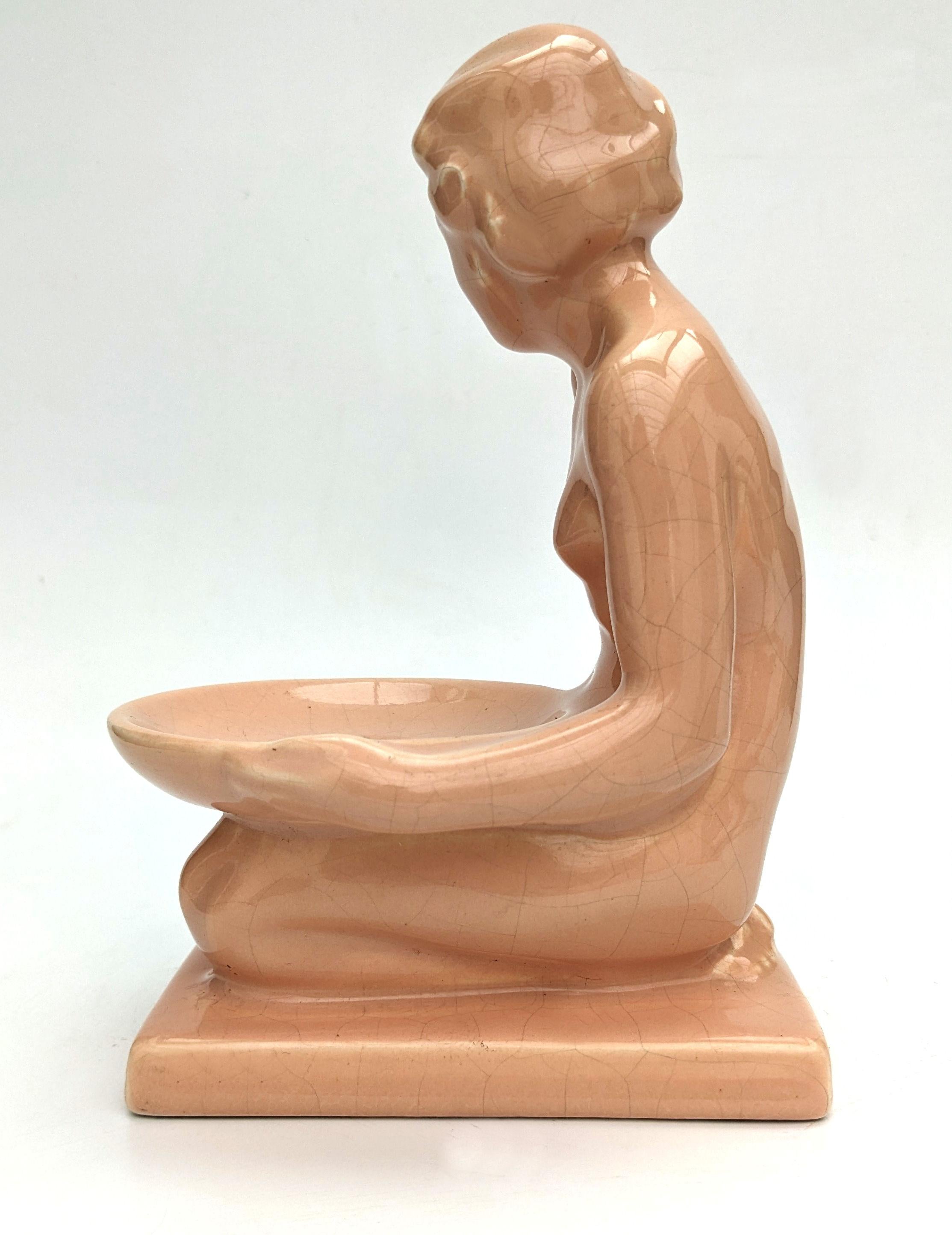 Wir bieten Ihnen diese charmante Art Deco Keramikfigur, die ein nacktes junges Mädchen mit einer flachen Schale auf dem Schoß darstellt. Diese Figur hat eine tolle Größe und kann so ausgestellt werden, wie sie ist, oder man kann sie als Seifenschale