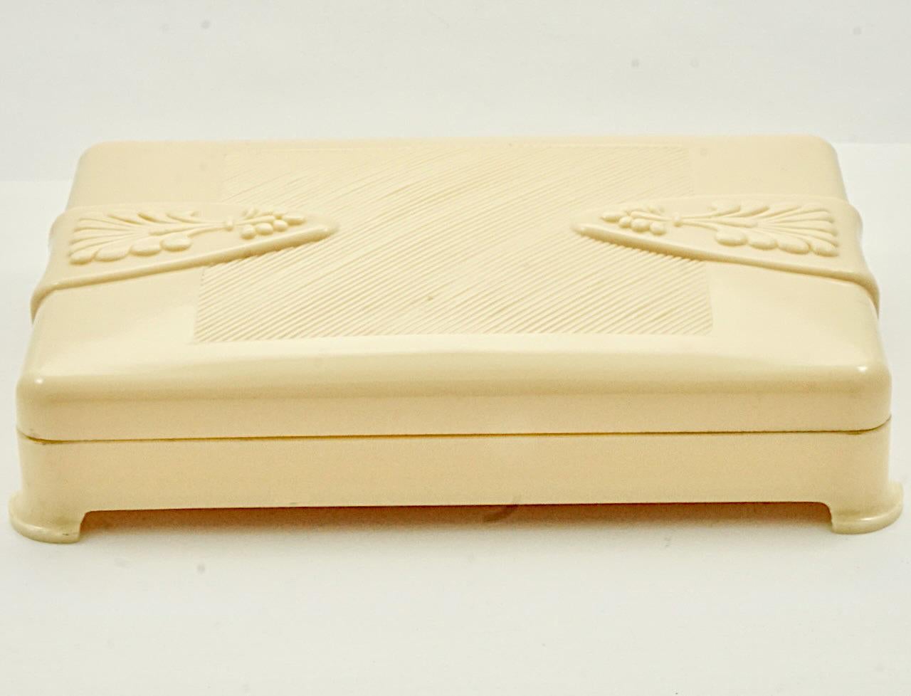 Schöne Art Deco Creme Zelluloid-Box. Länge 14,3 cm / 5,6 Zoll, Breite 9,6 cm / 3,77 Zoll und Tiefe 2,7 cm / 1 Zoll. Der Deckel ist mit einem schönen Prägedesign versehen. Die Box ist in sehr gutem Zustand. Es gibt einen Riss auf der