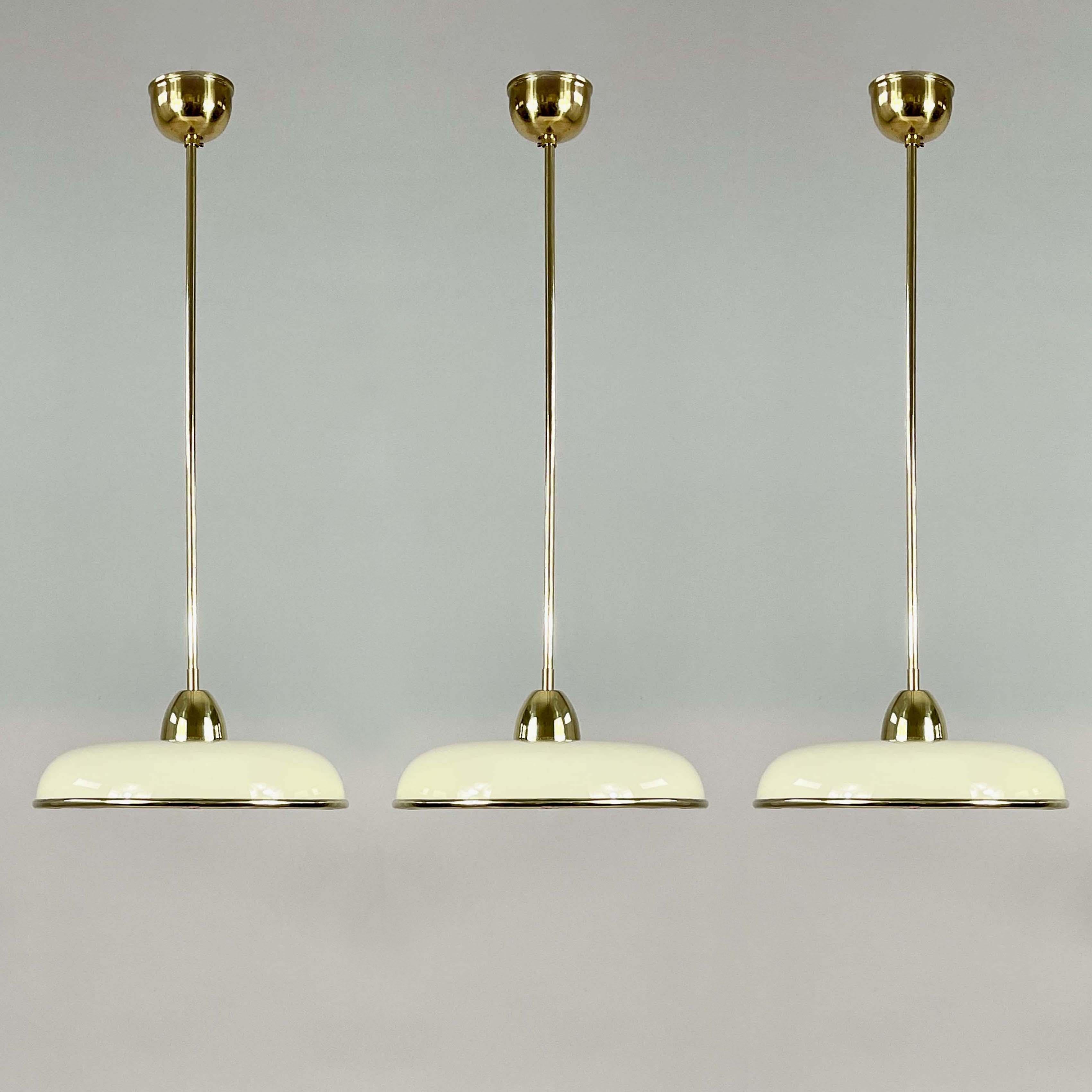 These ceiling fixtures were designed and manufactured in Germany in the 1930s.

The lights feature elegant domed cream colored opaline glass shades  suspended from slender polished brass rods and matching ceiling canopies. 

Their clean, symmetrical