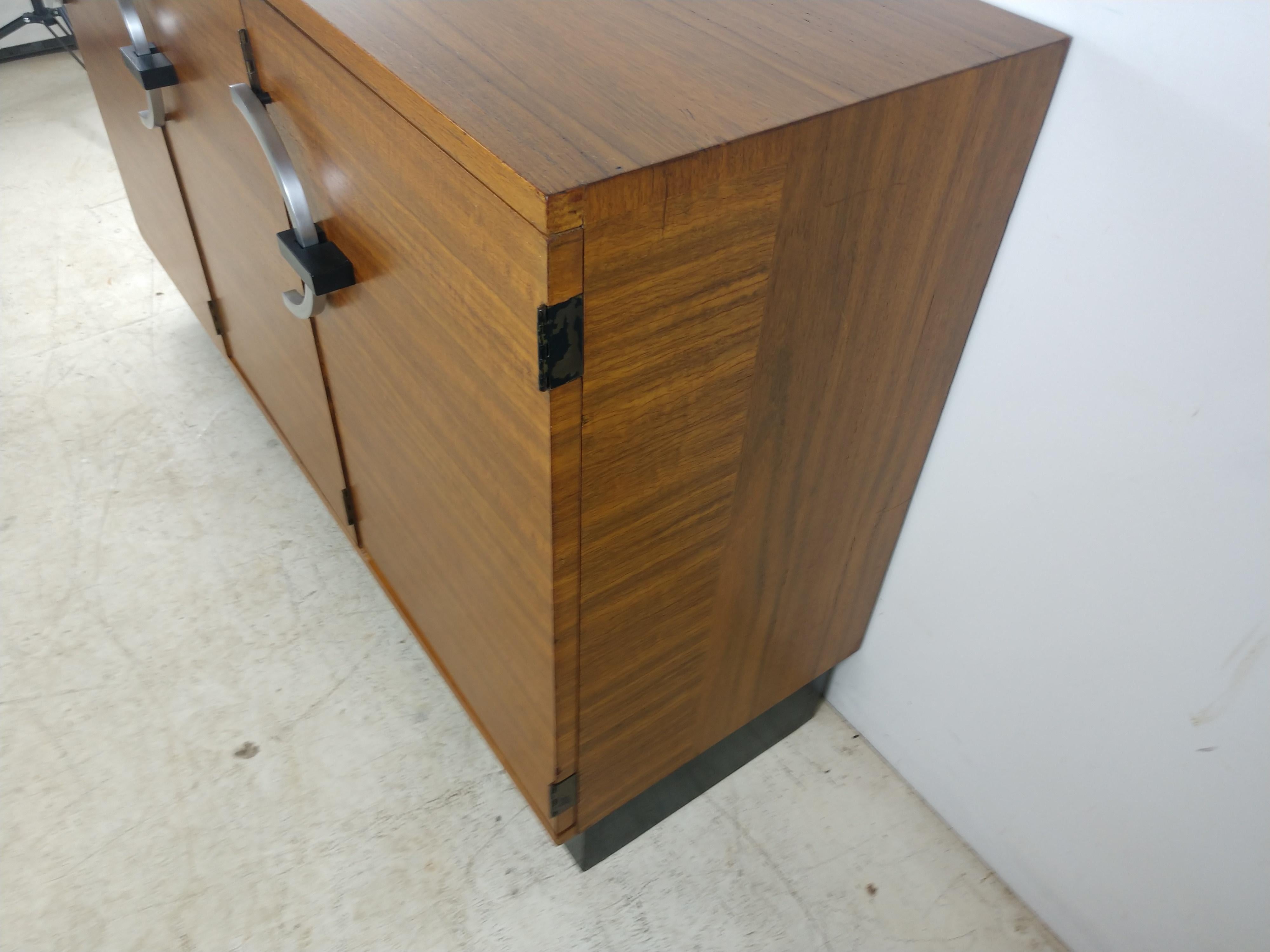 Fabulous and hard to find three drawer walnut cabinet. Early Gilbert and Herman Miller collaboration C1930. Left door opens to reveal a shelf and a slotted holder on the door. Middle door hides two small pullout drawers for tableware and two larger