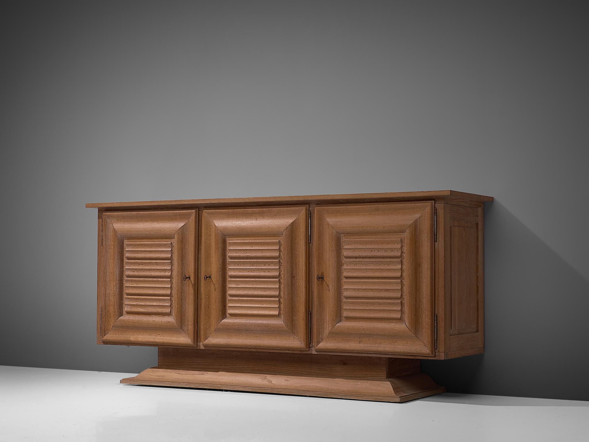 Credenza, in oak and metal, France, 1940s. 

French Art Deco style cabinet in cerused oak. This sturdy pedestal sideboard features three doors on the front that decorated and bordered with a wooden square frame. The front features three dimensional