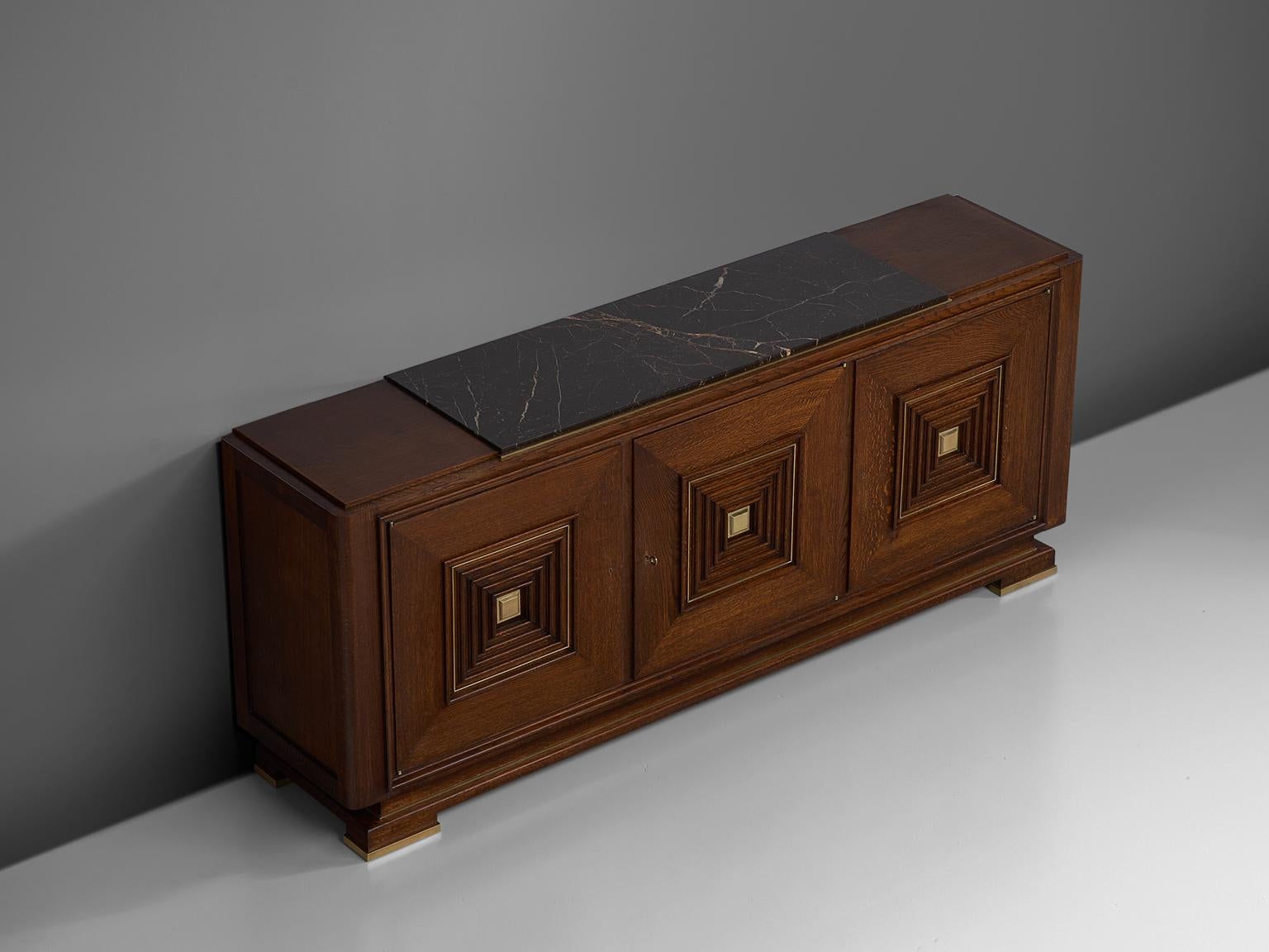 Credenza, in oak marble and brass, France, 1930s. 

Large Art Deco sideboard in the style of Maxime Old. This heavy, almost Brutalist, credenza seems to float on its elegant base with stunning brass detailing. The credenza is equipped with three