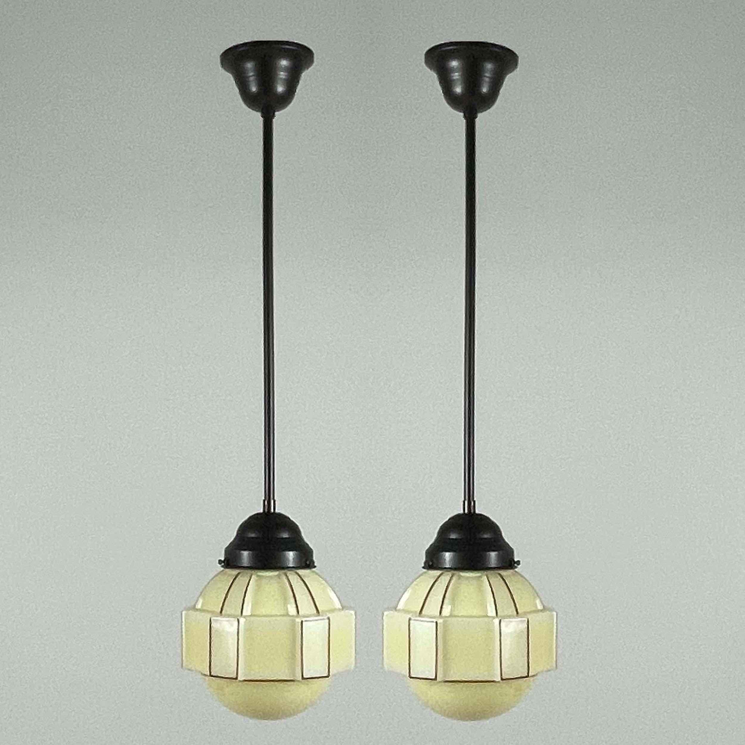 Cet ensemble inhabituel de pendentifs Art déco a été conçu et fabriqué en Suède dans les années 1930. Les lampes sont dotées d'un abat-jour en opaline de couleur crème avec un décor rouge et des ferrures en laiton bruni/bronzé.

Les lampes