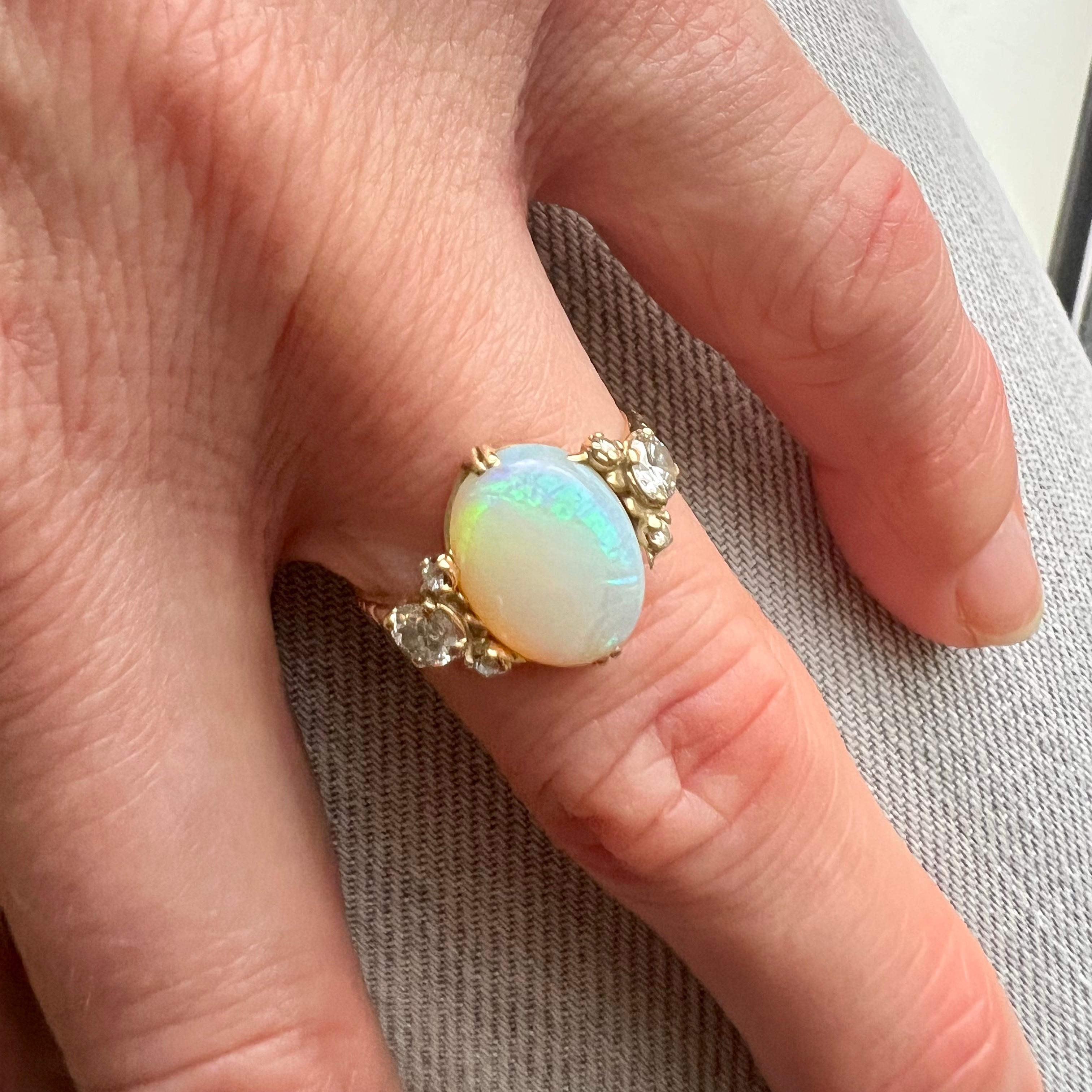 This Art Deco opal and diamond ring features a glowing crystal white oval opal created with a trio of bright white brilliant cut diamonds on either side of this beautiful ring. The shank of the ring is made of 14 karat yellow gold and crafted with