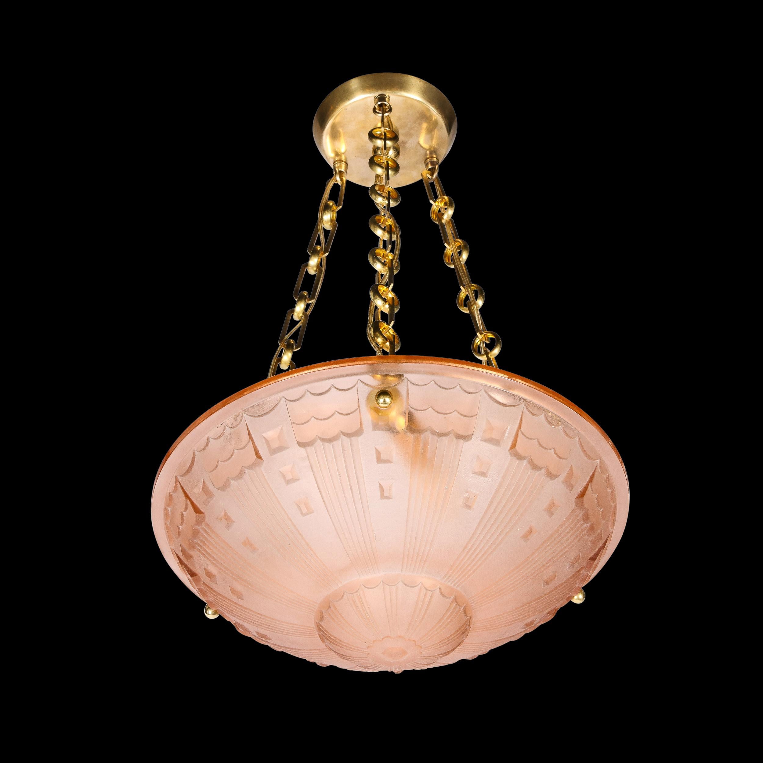 Ce lustre pendentif Art déco raffiné en verre rose dépoli avec des accessoires en laiton provient de France, vers 1930. Cette pièce est suspendue par trois magnifiques sections de chaîne en laiton composées de boucles alternées et de maillons aux