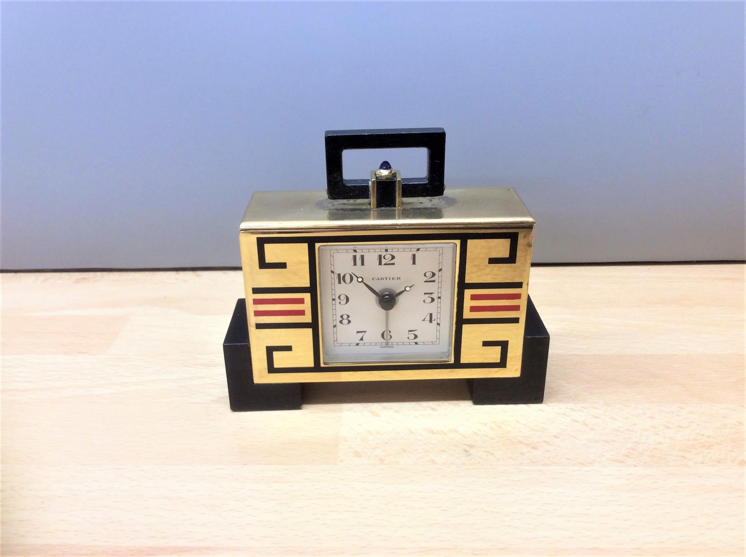 C A R T I E R



Art Deco ‘cubist’ travel clock in a gilded case resting on black block feet with black and red geometric line decoration.


Painted dial with Arabic numerals signed ‘Cartier’, original steel moonpoise hands with luminous centres and