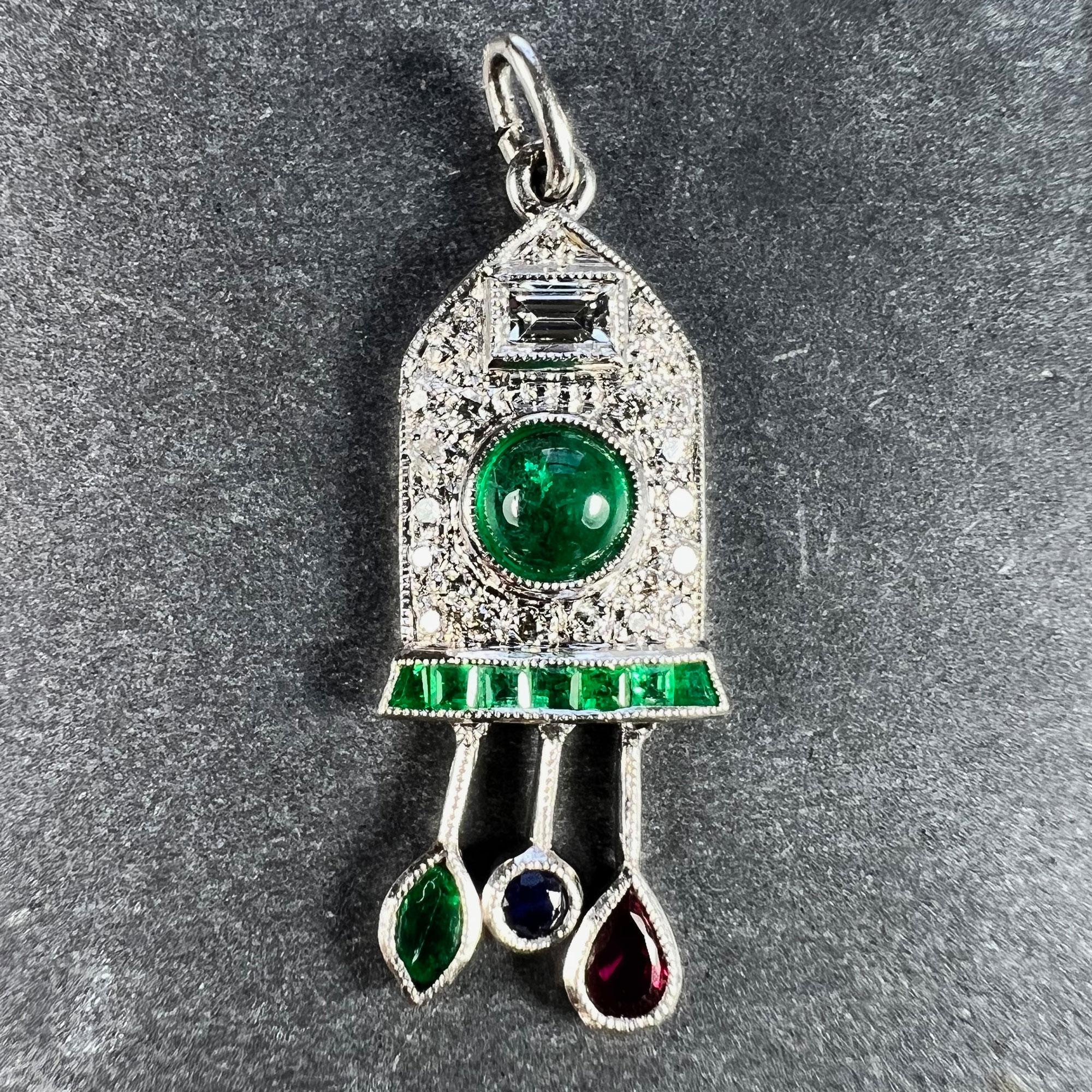 An Art Deco platinum charm pendant designed as a diamond and emerald cuckoo clock with sapphire, ruby and emerald weights and pendulum. Set with one emerald cut diamond and 21 round brilliant cut diamonds; one cabochon, 7 step cut and one marquise