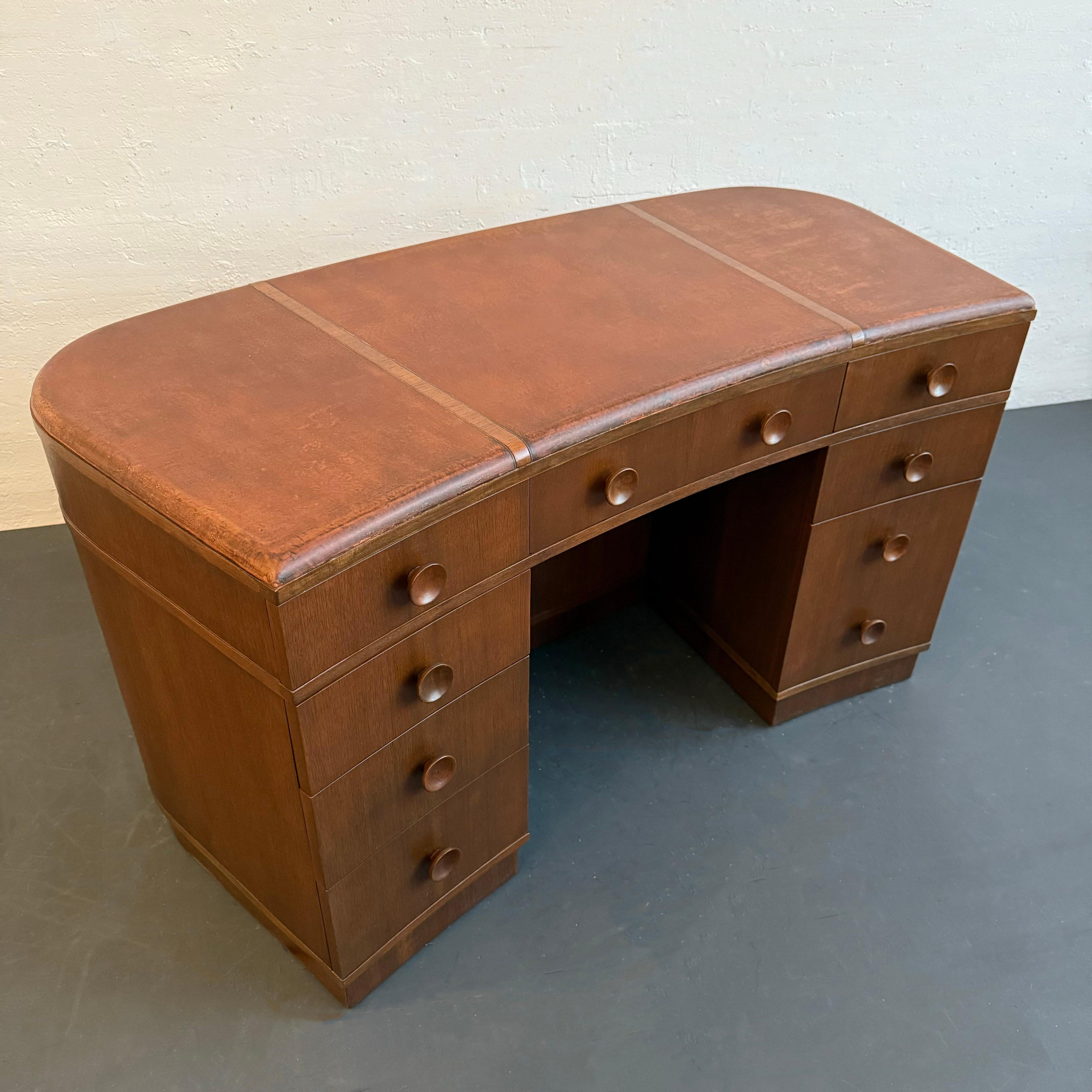 Este gran escritorio ejecutivo Art Decó de caoba, bellamente curvado, es una pieza majestuosa que llama la atención.  El escritorio tiene un tablero segmentado de cuero patinado, ocho cajones (un cajón para carpetas), cada uno con un elegante