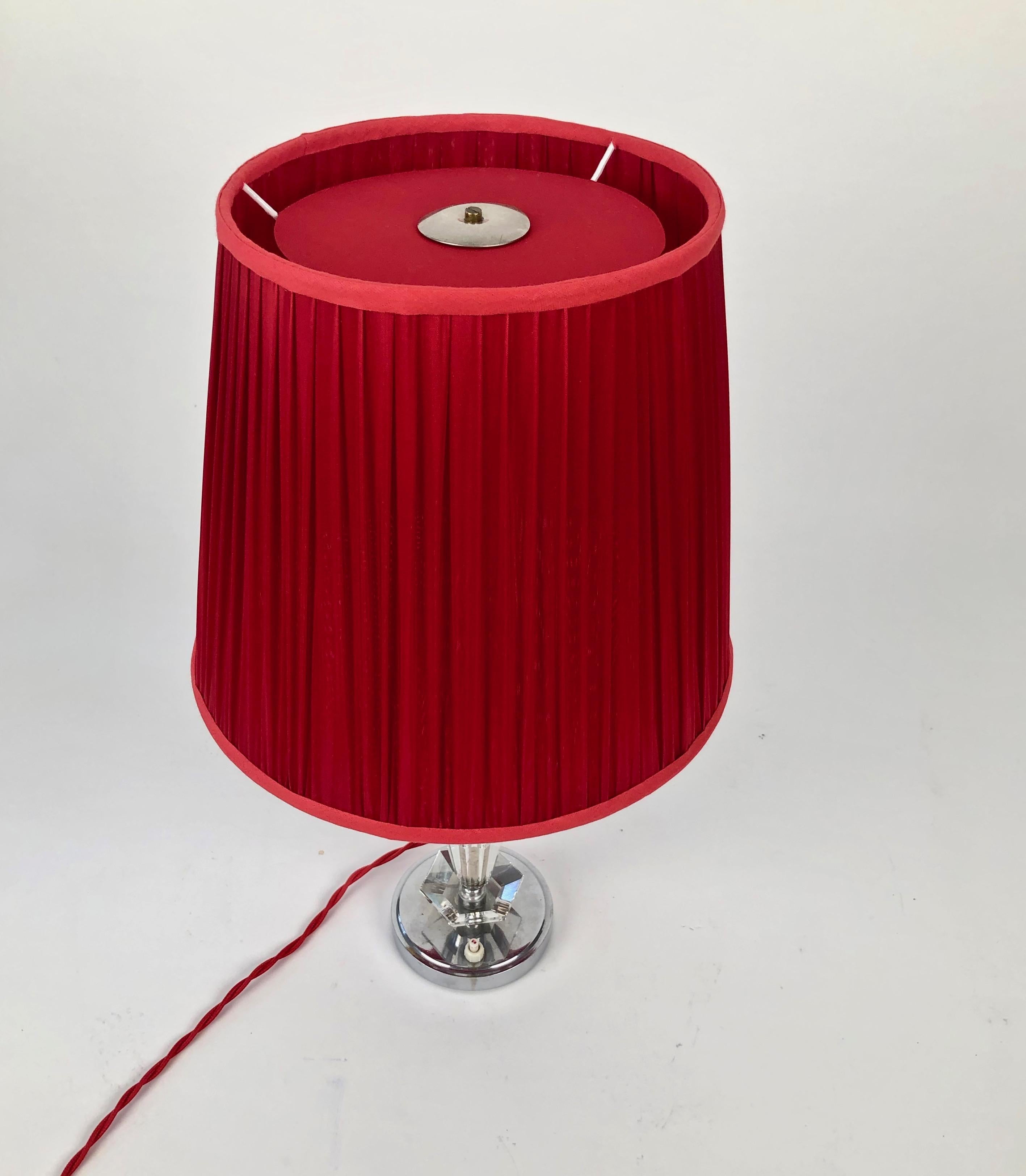 This is a beautiful cut glass table lamp from France. The geometrically cut glass elements
are composed in a elegant form. The red silk shade heightens the sensual form and is
complimented with a woven red textile cable from Italy.