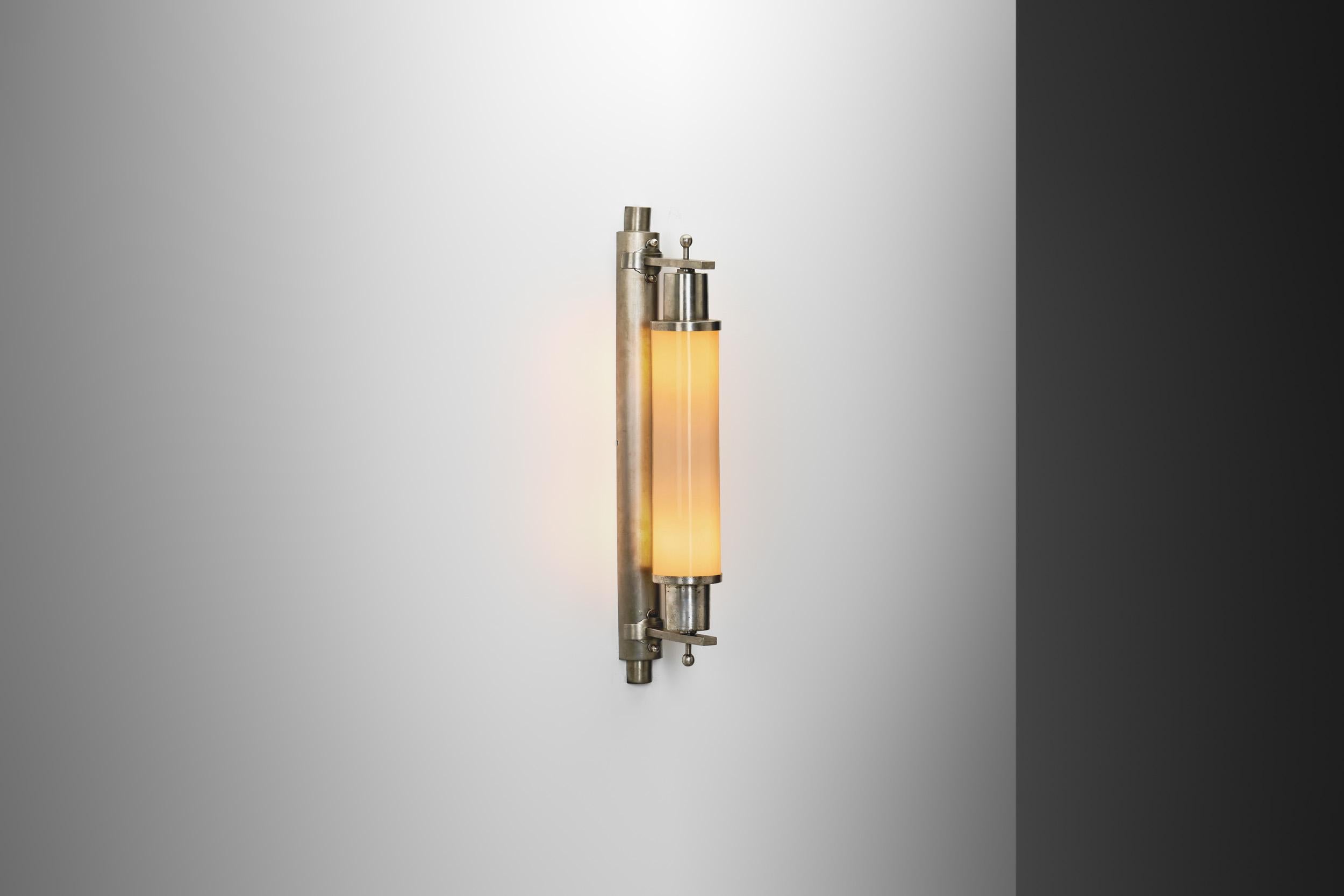 Questa lampada da parete cilindrica è la prova dell'inventiva e del fascino senza tempo dell'Art Déco. Questa lampada è stata progettata per offrire un'eleganza elegante e dinamica che simboleggiasse la ricca scena culturale dell'epoca in Europa e