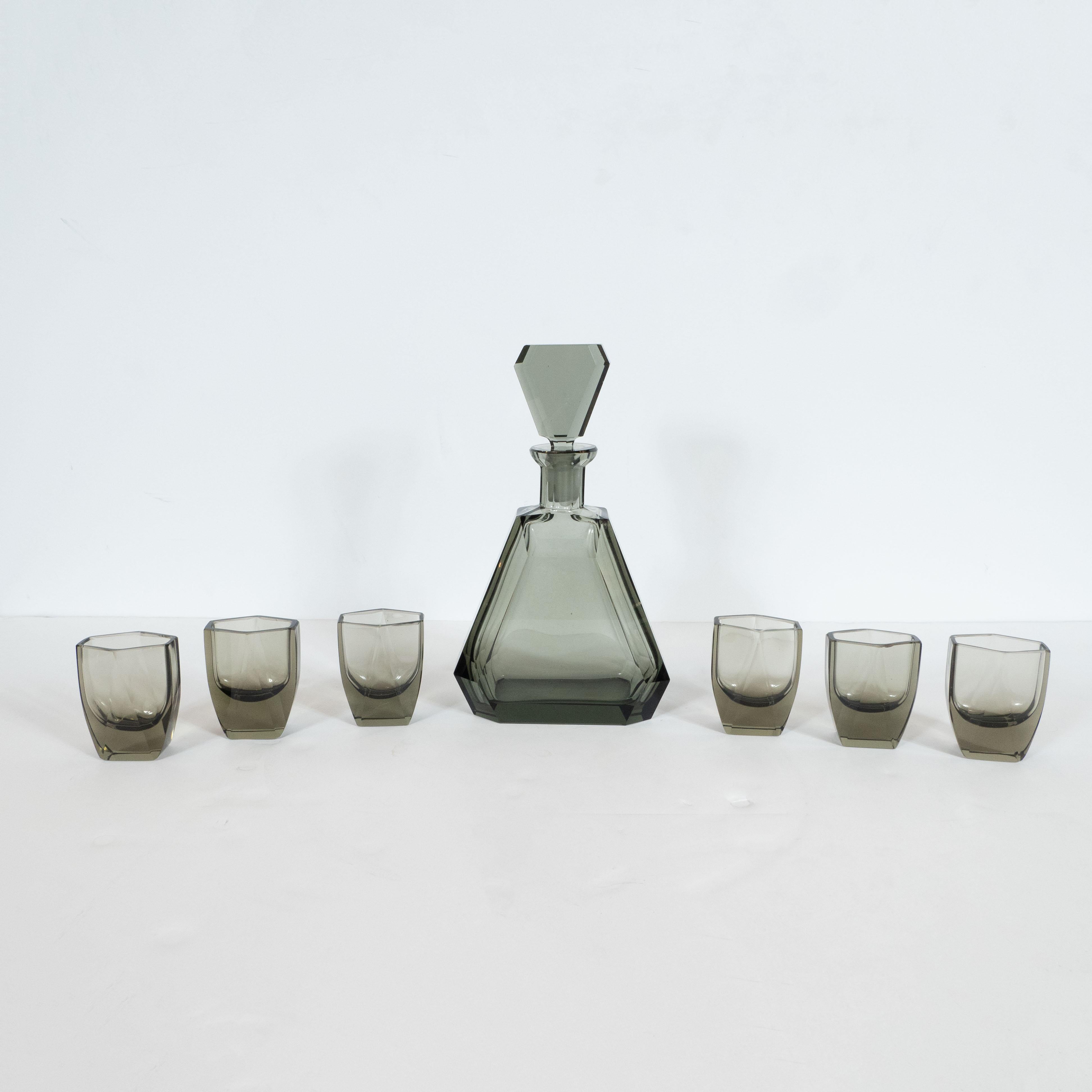 This elegant Art Deco machine age decanter set was realized in the Czechoslovakia, a country renowned for its superlative glass production during this period, circa 1935. It features a faceted decanter with its original stopper in sultry translucent
