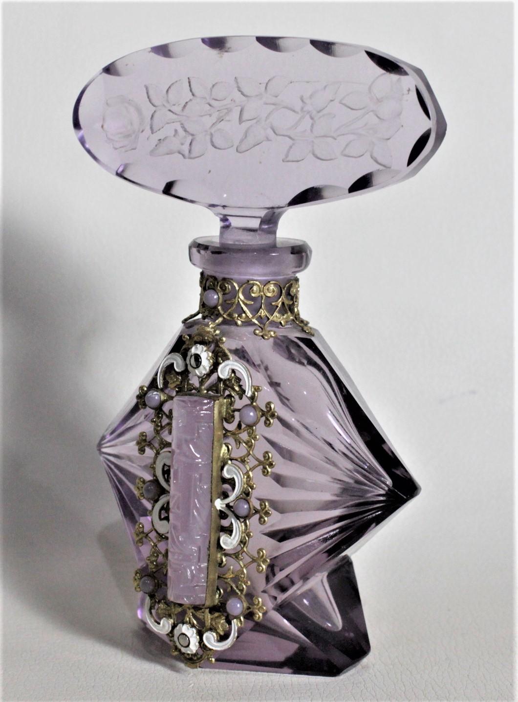 This Art Deco perfume or scent bottle is unsigned but presumed to have been made in Bohemia in approximately 1935. The glass is a deep purple with deep faceted sides and etched and cut top. The bottle features an ornate gold toned filigree collar