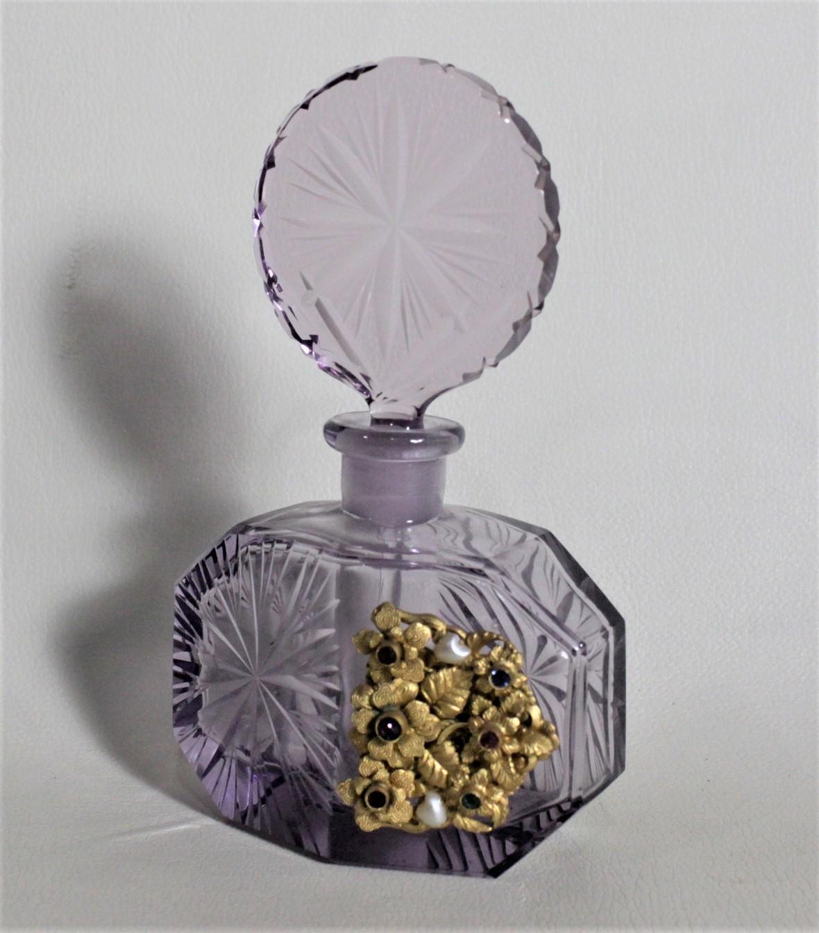 This Art Deco perfume or scent bottle is unsigned, so the artist cannot be identified, but was made in Bohemia in circa 1935. The glass is a deep purple with deep faceted sides and etched and cut top. The bottle features an ornate gold toned