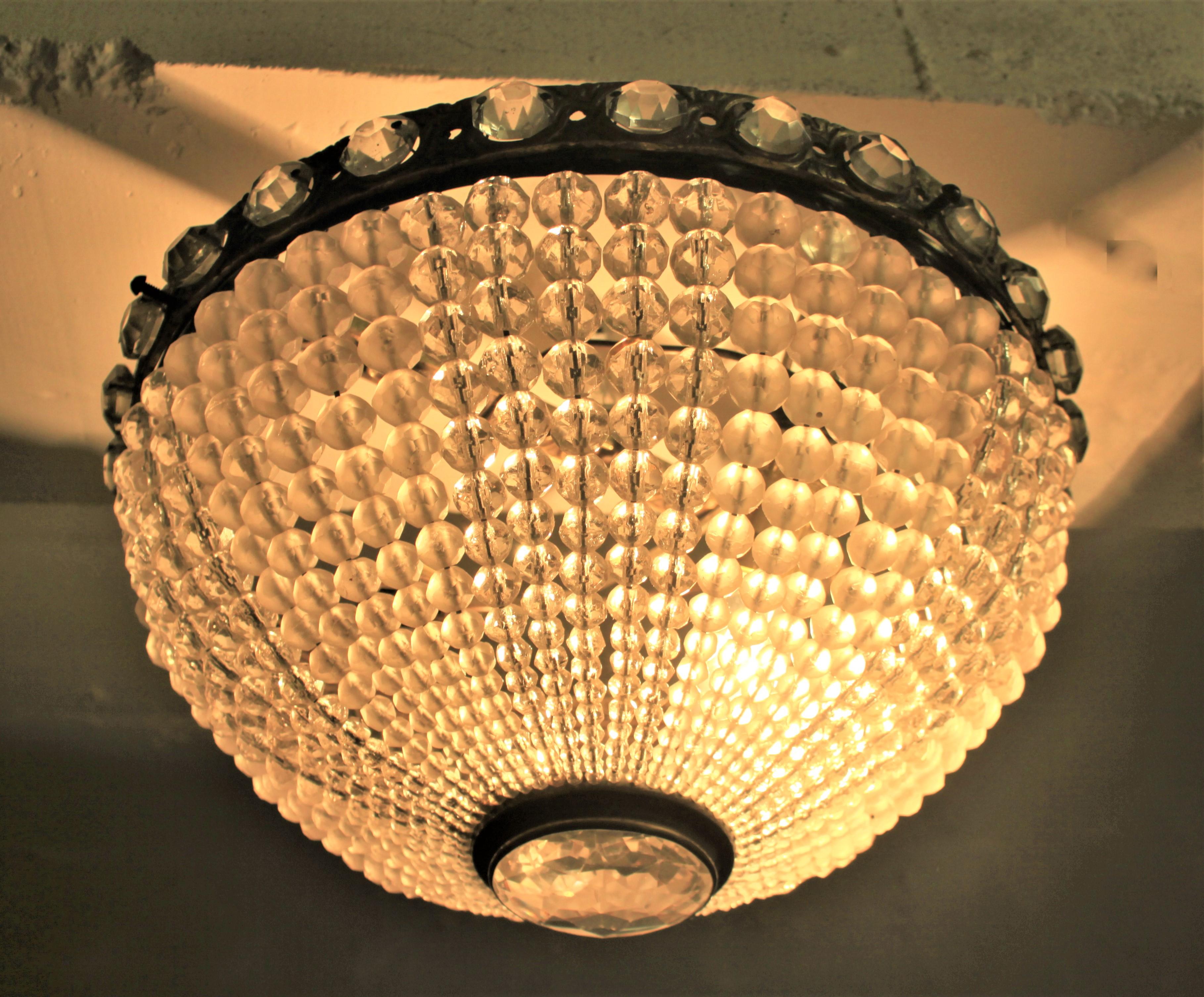 Presumed to have been made in the Czech Republic, this beaded and beveled crystal flush mount ceiling fixture is done in the Art Deco period and style. The bronze ring surround is intricately cast with scroll decoration which accent the numerous