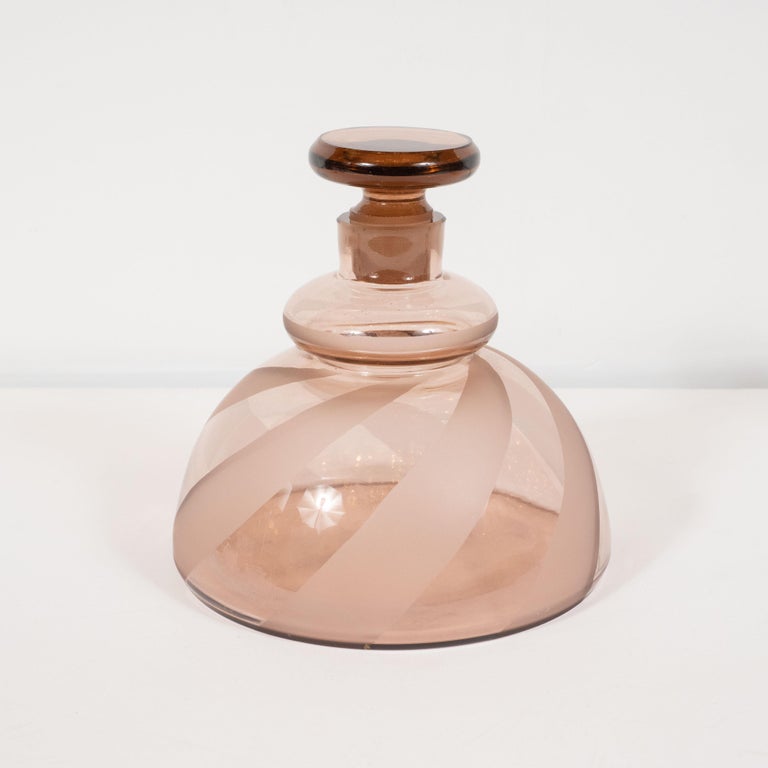 This beautiful Art Deco decanter set was realized in Czechoslovakia- one of the finest producers of glass objects of the era, circa 1930. It features a decanter and four glasses in a rich smoked rose hue. The decanter offers a domed concave form