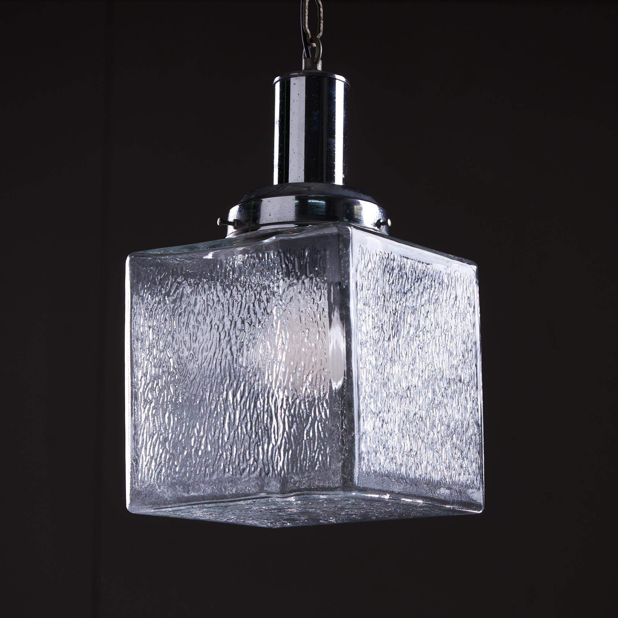 Ce magnifique pendentif a la forme d'un parallélépipède et est fabriqué en verre pommelé, ce qui lui confère un aspect unique et artistique qui se démarque vraiment. Il présente un corps chromé avec des signes mineurs d'âge et d'utilisation, ce qui