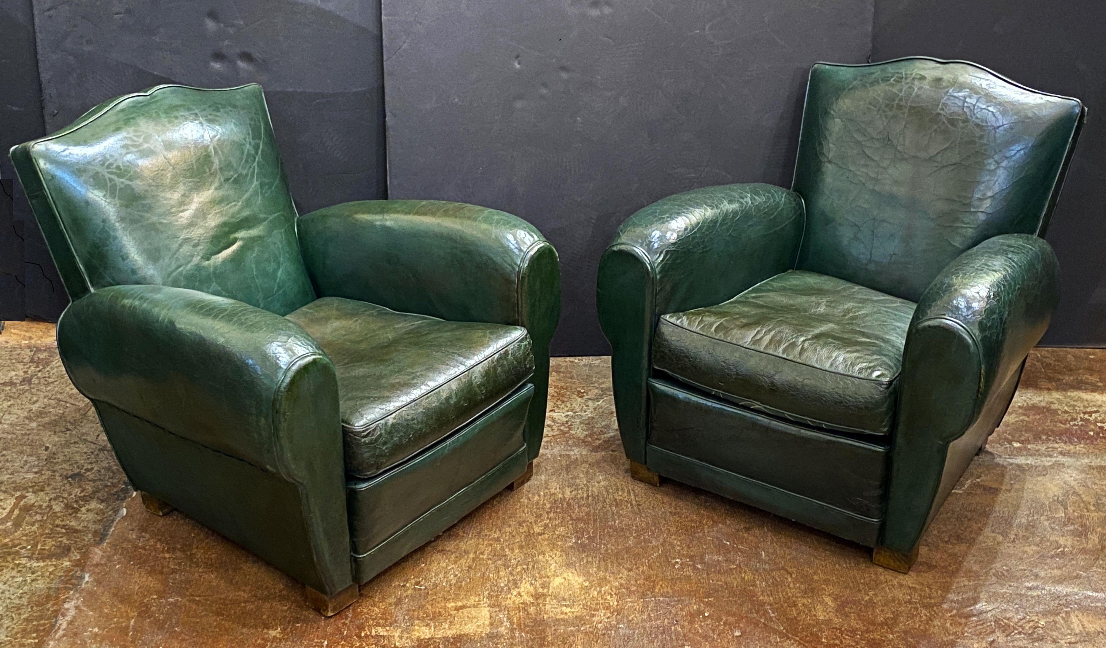 A pair of handsome vintage French club or lounge chairs from the Art Deco era, upholstered in a dark green leather - each chair featuring a comfortable shaped back and seat with removable cushion, with stylish arms and original leather, brass