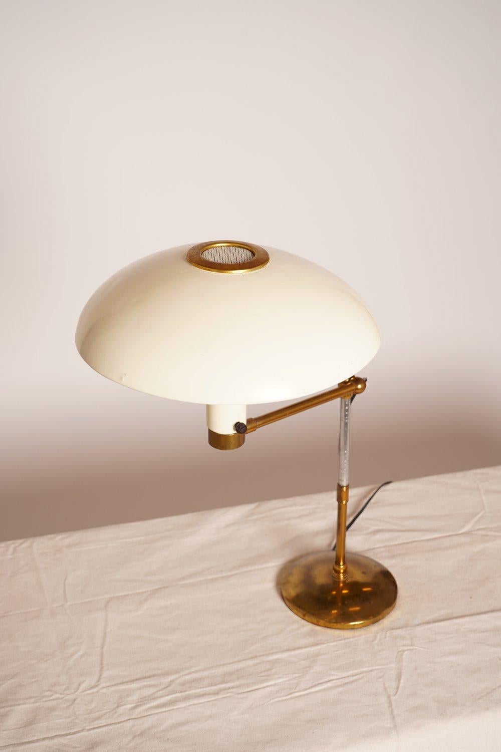 This Art Deco Dazor swing arm brass desk lamp features a metal reflector saucer shade with perforation, adjustable stem, swing arm, brass details and bright brass 6.5D base.
