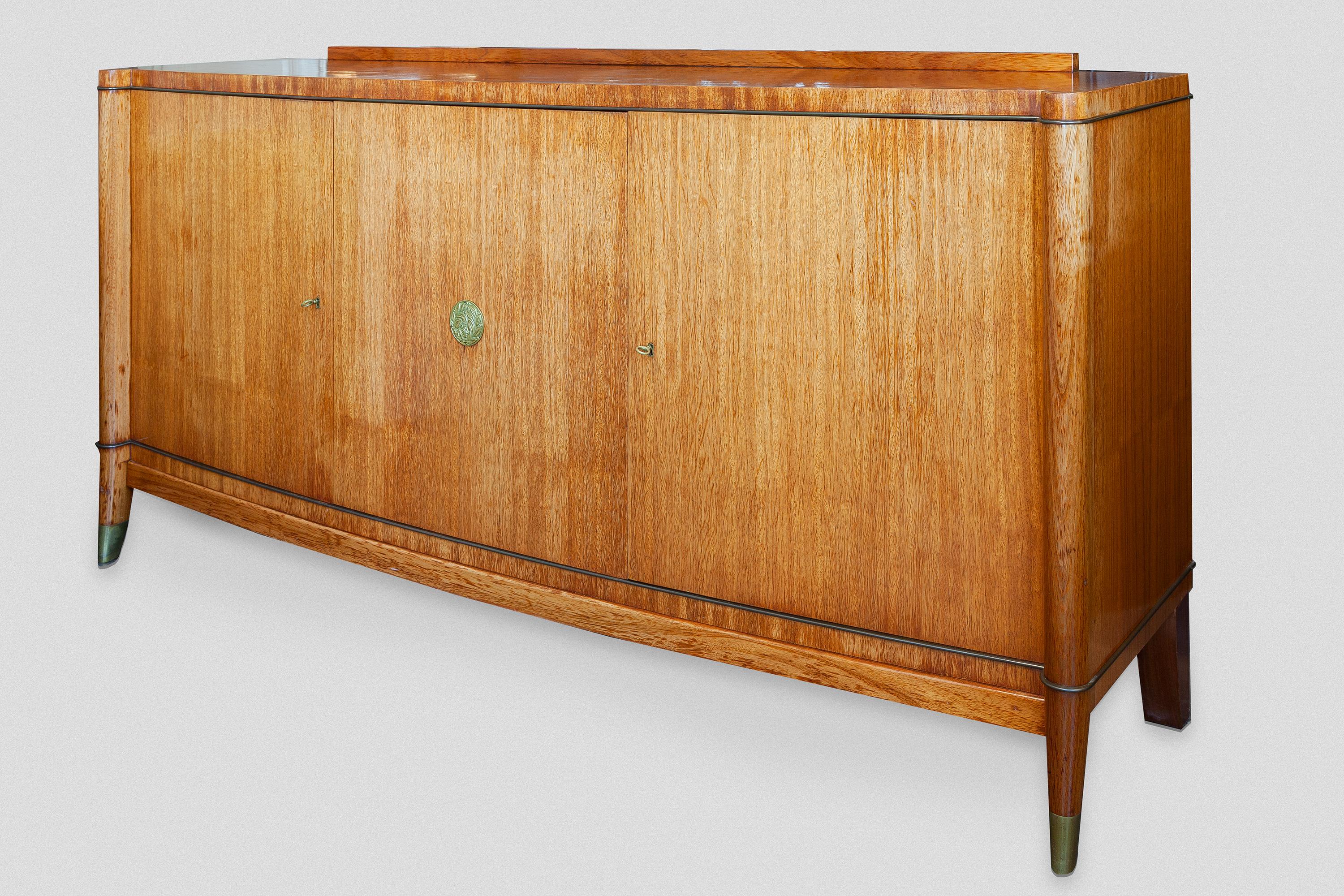 An elegant and high quality of craftsmanship 1940s three-door bow front sideboard by De Coene Frères, Belgium. The bow-front sideboard executed with three doors centering bronze medallion flanked by plain pilasters ending in splayed supports with