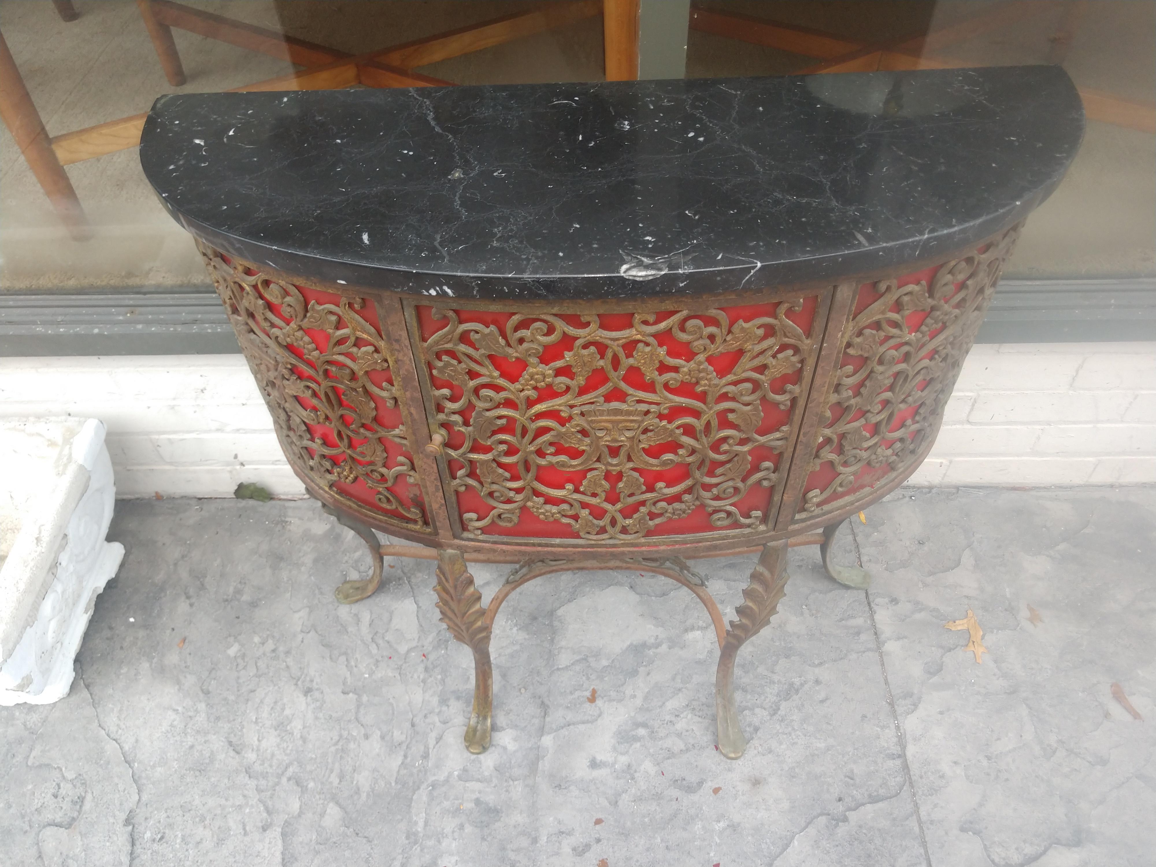 Exceptional console cabinet table with fabulous iron work in the form of grape leaf and vine with masquerade faces in the center of each panel. Gilt iron with a red interior which originally housed a radio. Has a back door for all cords to exit. In