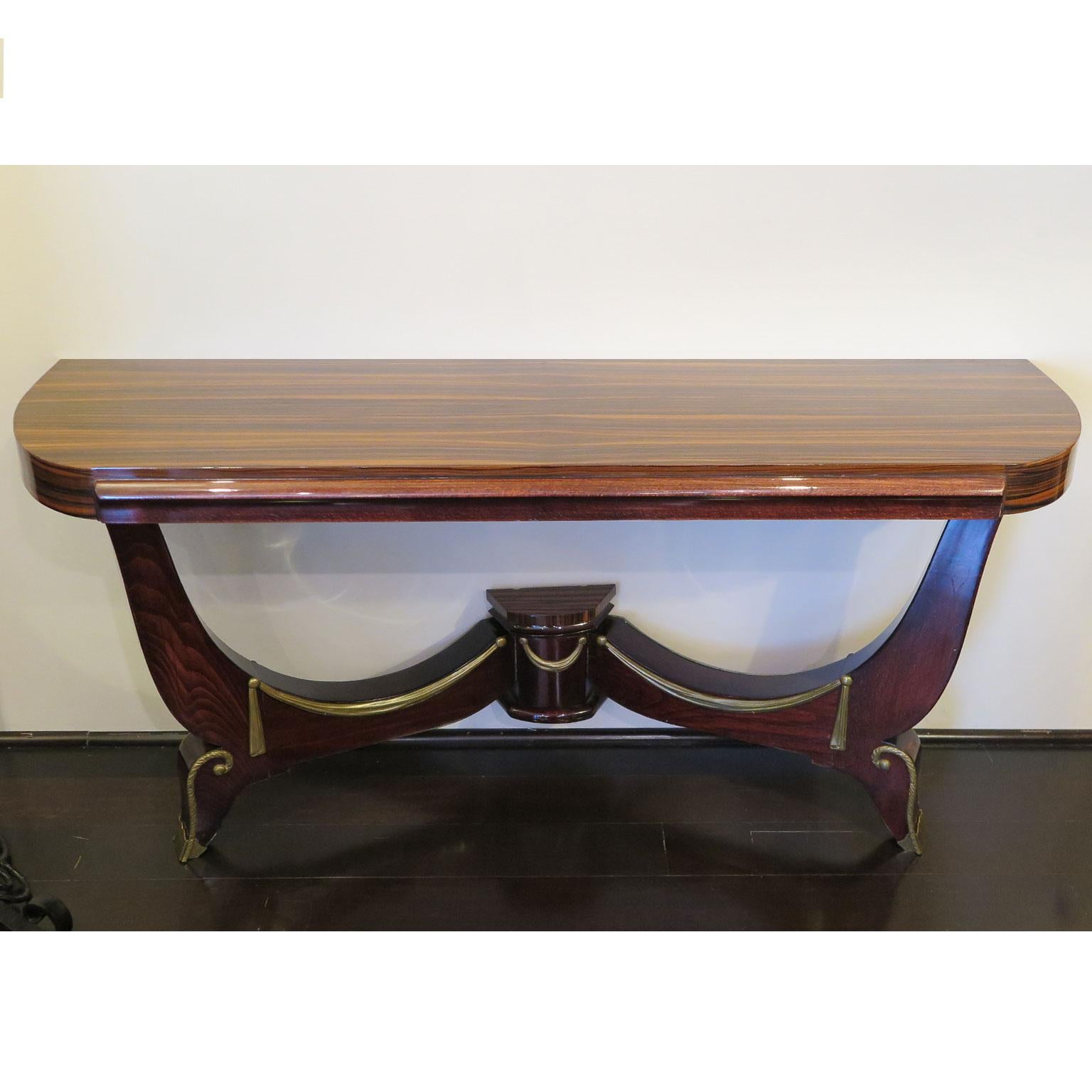 Classic Art Deco console showcases a demilune top. The top and base detail is done in Macassar while the curved legs and front apron are in a Mahogany. The curved base features brass details in the style of tassels and swirl details on the feet with