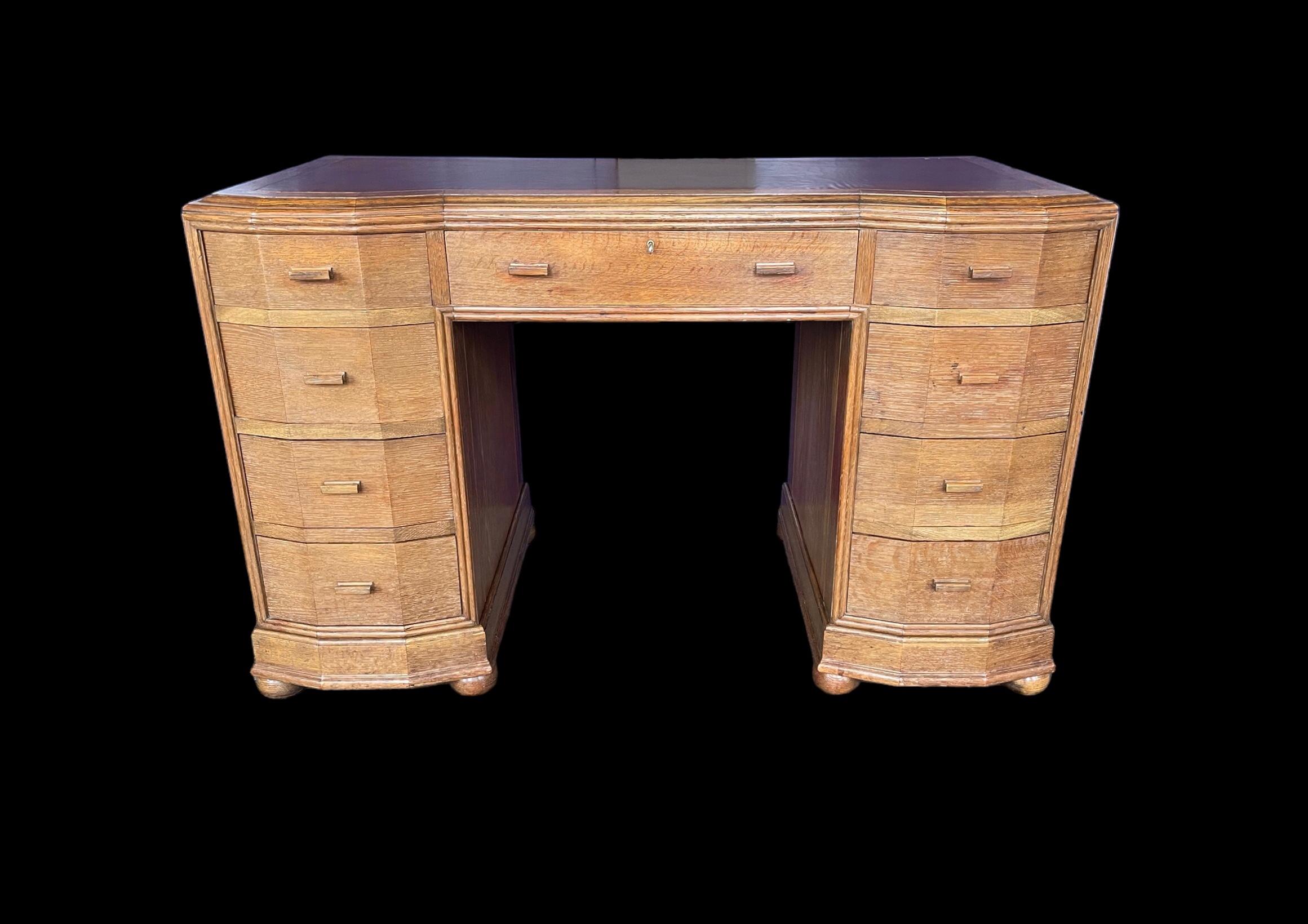An Art Deco light oak nine drawer, bar handled, inverted breakfront twin pedestal desk. Just fitted with a new leather top. The central drawer with a working lock and key. A quality, heavy desk from the 1930’s with dovetail joints to each drawer and