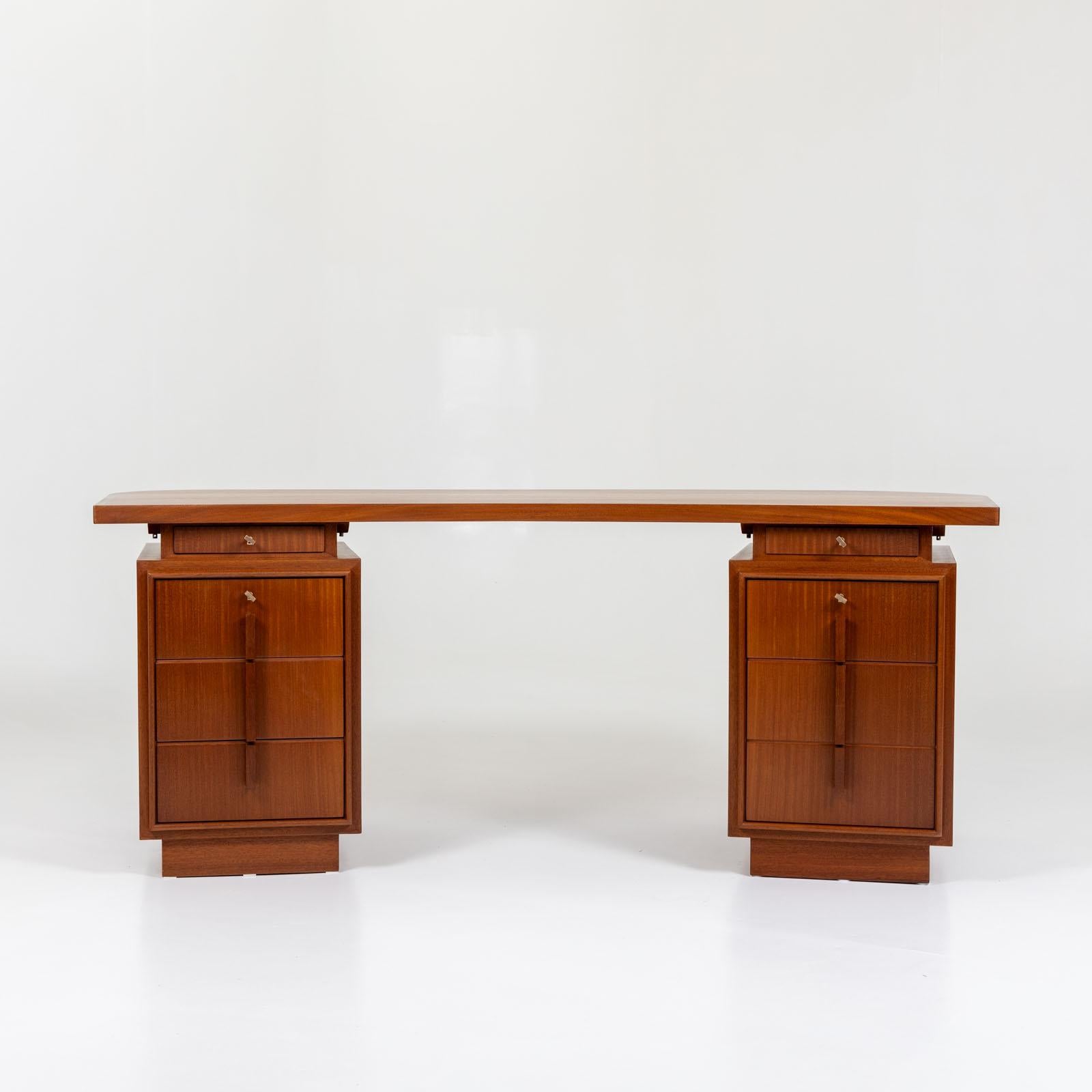 Art Deco desk with slightly curved table top and two drawer elements with four drawers each. These are lockable and the handles are made of elegant bars. The desk can be positioned anywhere in the room thanks to the fully veneered back.  