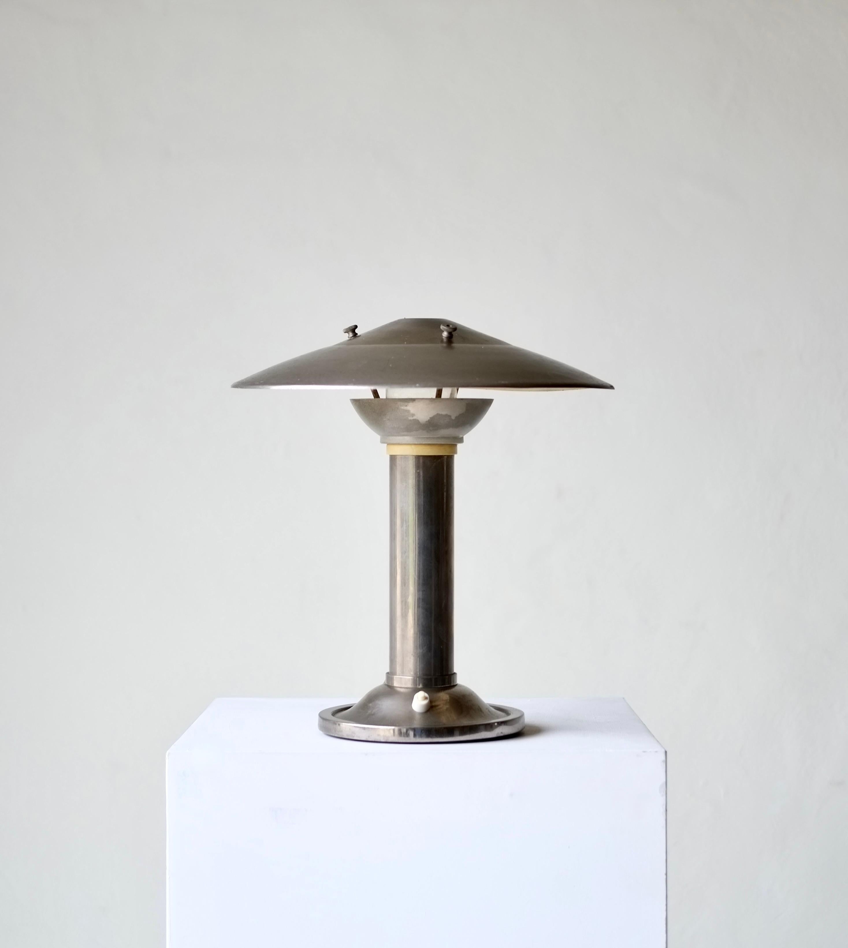 Art Deco lamp by Eloctra and attributed to George Halais.

France, circa 1930's.

Tarnished metal with slight warping to one side of the shade. 

H 33 Dia 32 cm