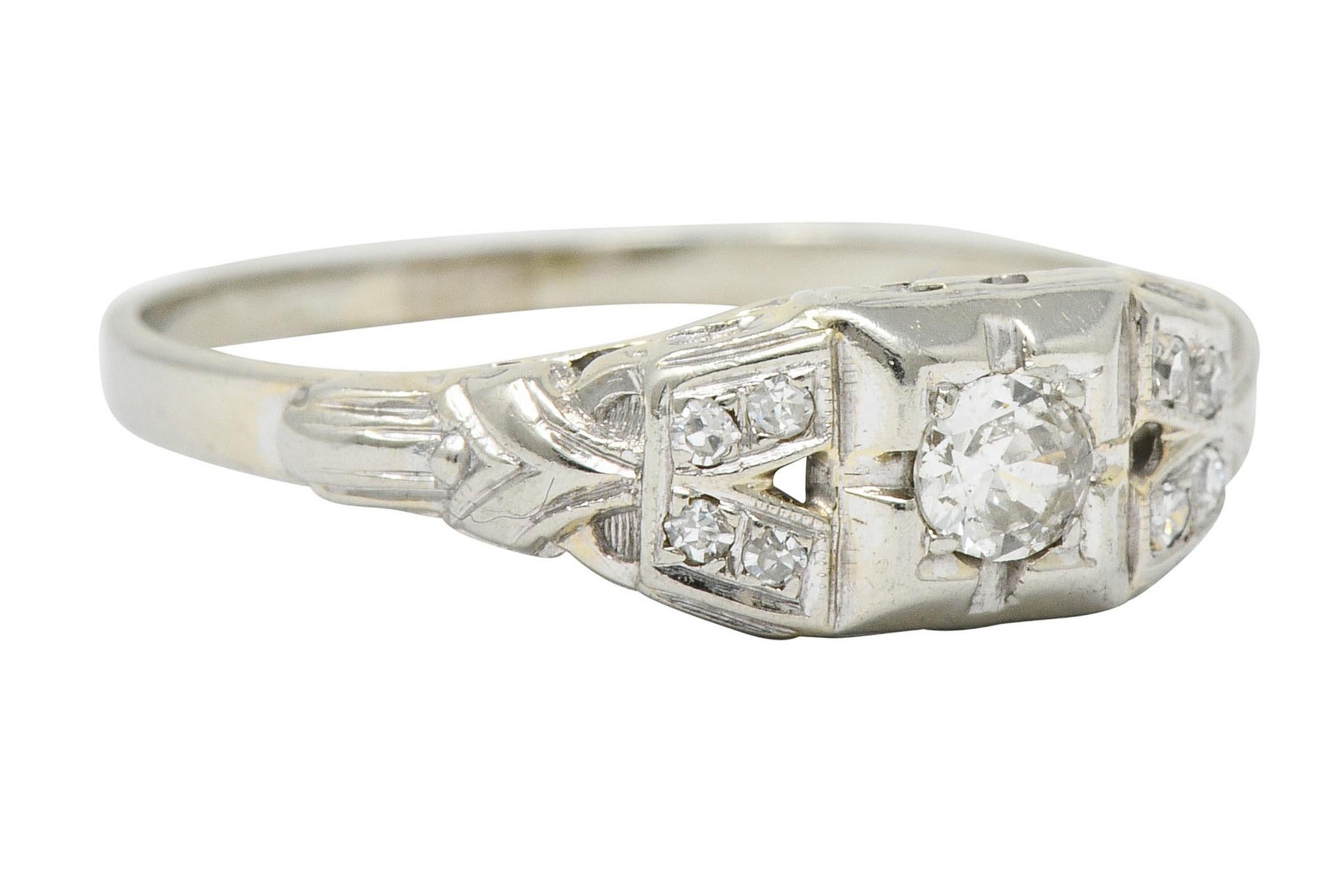 Centering a transitional cut diamond weighing approximately 0.15 carat; J color and SI clarity

Set low in a stylized square form head and flanked by V shaped shoulders, deeply engraved

Accented by single cut diamonds weighing approximately 0.10