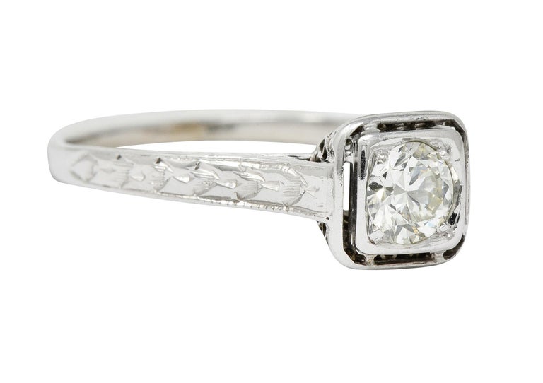 Centering a transitional cut diamond weighing approximately 0.45 carat; J color with VS clarity

Set low in cushion shaped mounting with an intricately pierced trellis gallery

Completed by cathedral shoulders deeply engraved with a foliate
