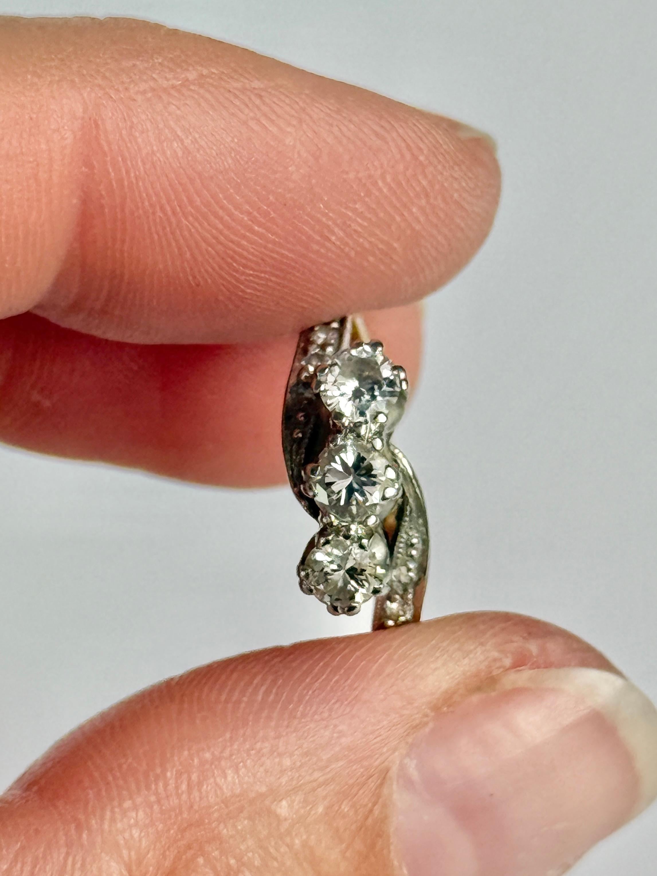 This diamond ring holds three glittering diamonds measuring a total of 60pts and the shoulders also have smaller diamonds set within them measuring 2pts each. Set in platinum twist settings and ring modelled in 18 Carat gold. 

Ring Size: J or 4
