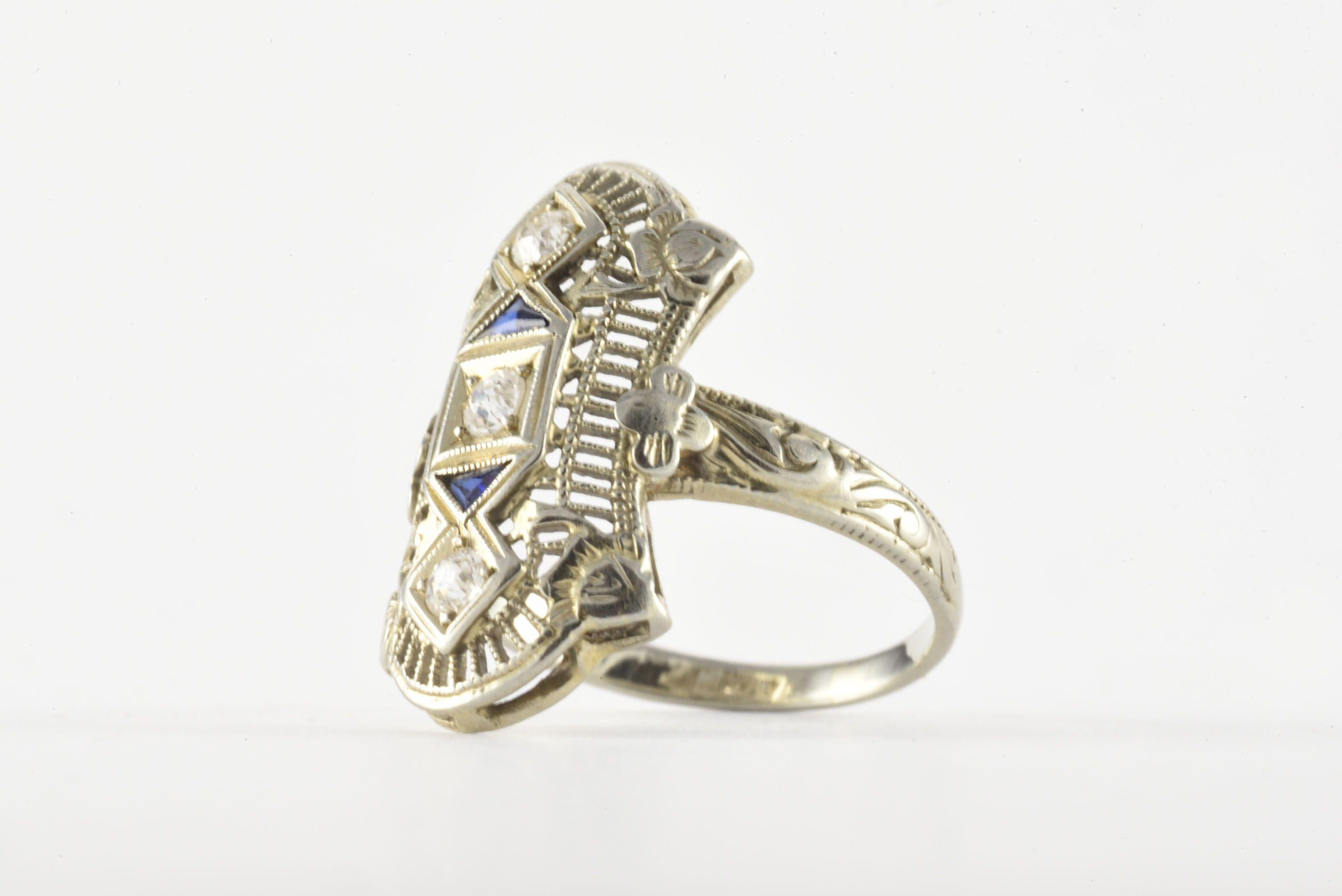 Crafted in the 1920s, this Art Deco Navette-shaped band fashioned from 18kt white gold features a trio of Old European cut diamonds, G-H color, VS-SI clarity, totaling approximately 0.15 carats and accented by two trillion-shaped blue sapphires and