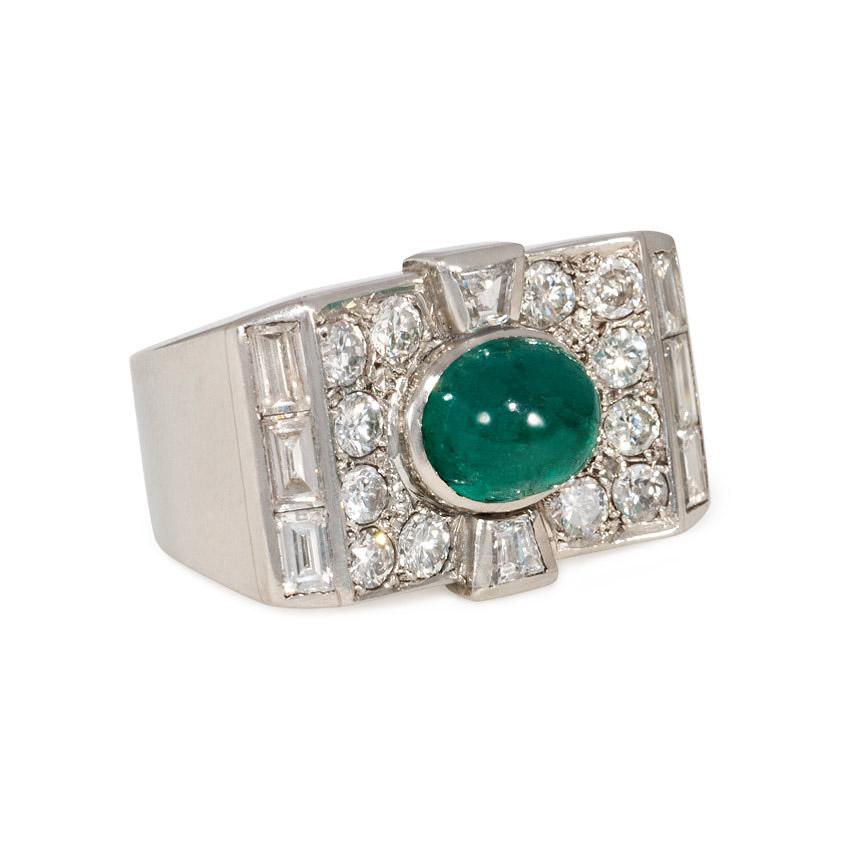 An Art Deco diamond ring of plaque-shaped and slightly concave rectangular design, set with a central cabochon emerald, baguette diamond borders, and trapezoid diamond accents, in platinum. Emerald is approximately 2.13 cts.; atw 1.36 ct. diamonds. 