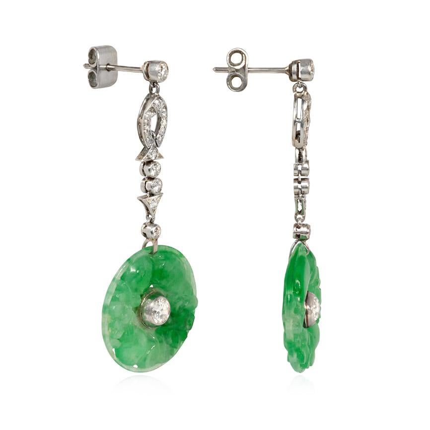 A pair of Art Deco earrings comprised of carved jade disk pendants suspending from diamond surmounts, in platinum.