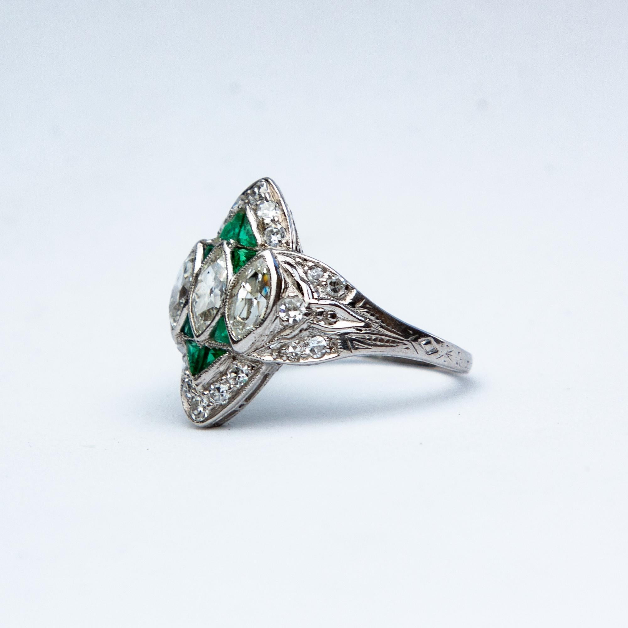 A wonderful example of an Art Deco marquise ring. With three central marquise shaped diamonds meauring point six carats each (1.8 total) set in platinum with diamond and emerald accents. 
Size: K 5 1/4
Head: 16.53 x 14.62mm
Weight: 3.3g
Color: G