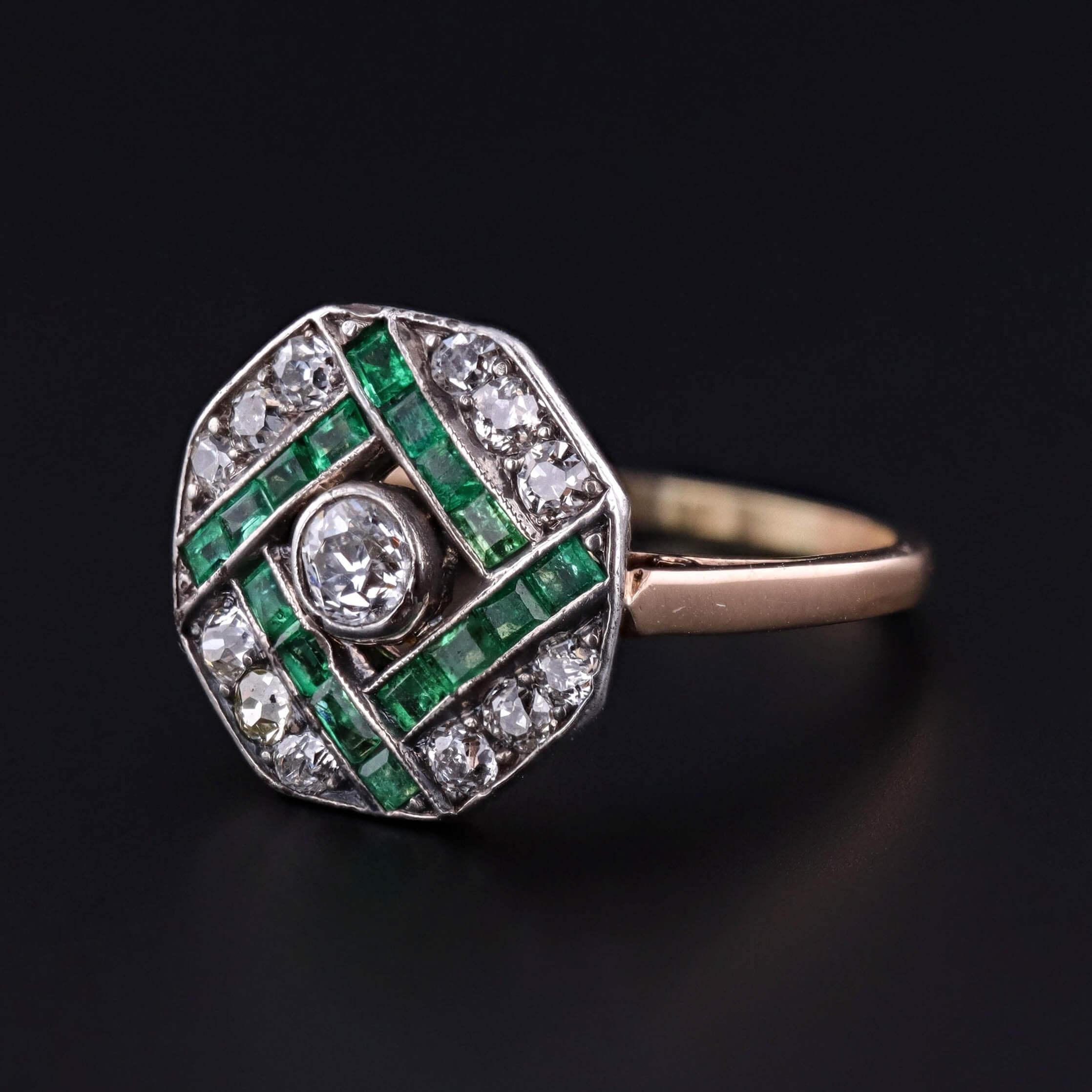A refined Art Deco ring, circa 1920, featuring a geometric arrangement of channel set emeralds and old cut diamonds set in silver, resting atop a 14k gold mounting. The clean lines, contrasting metals, and vibrant green-to-white palette capture the