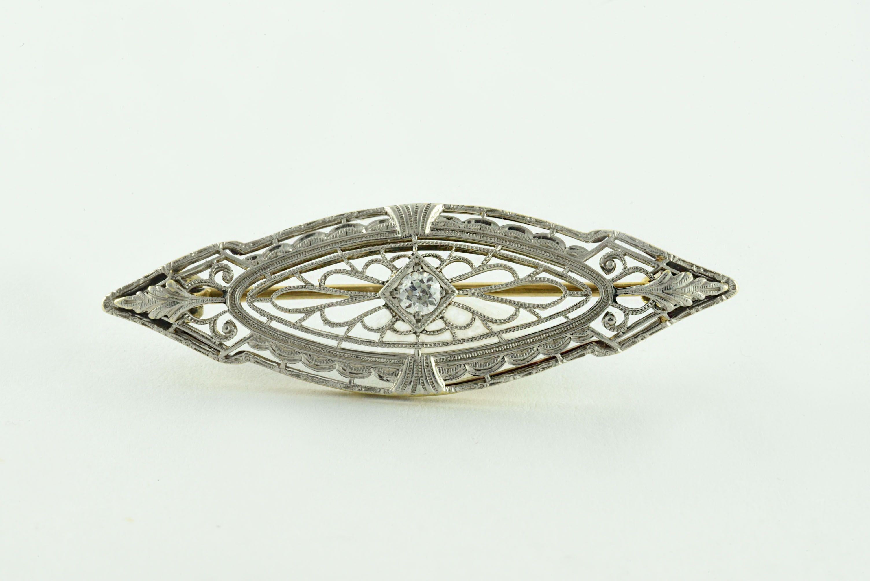 An Old European cut diamond weighing approximately 0.15 carats, G color, VS clarity, centers this stunning two-toned Art Deco brooch with delicate filigree, fashioned in 14kt yellow gold and platinum. 
