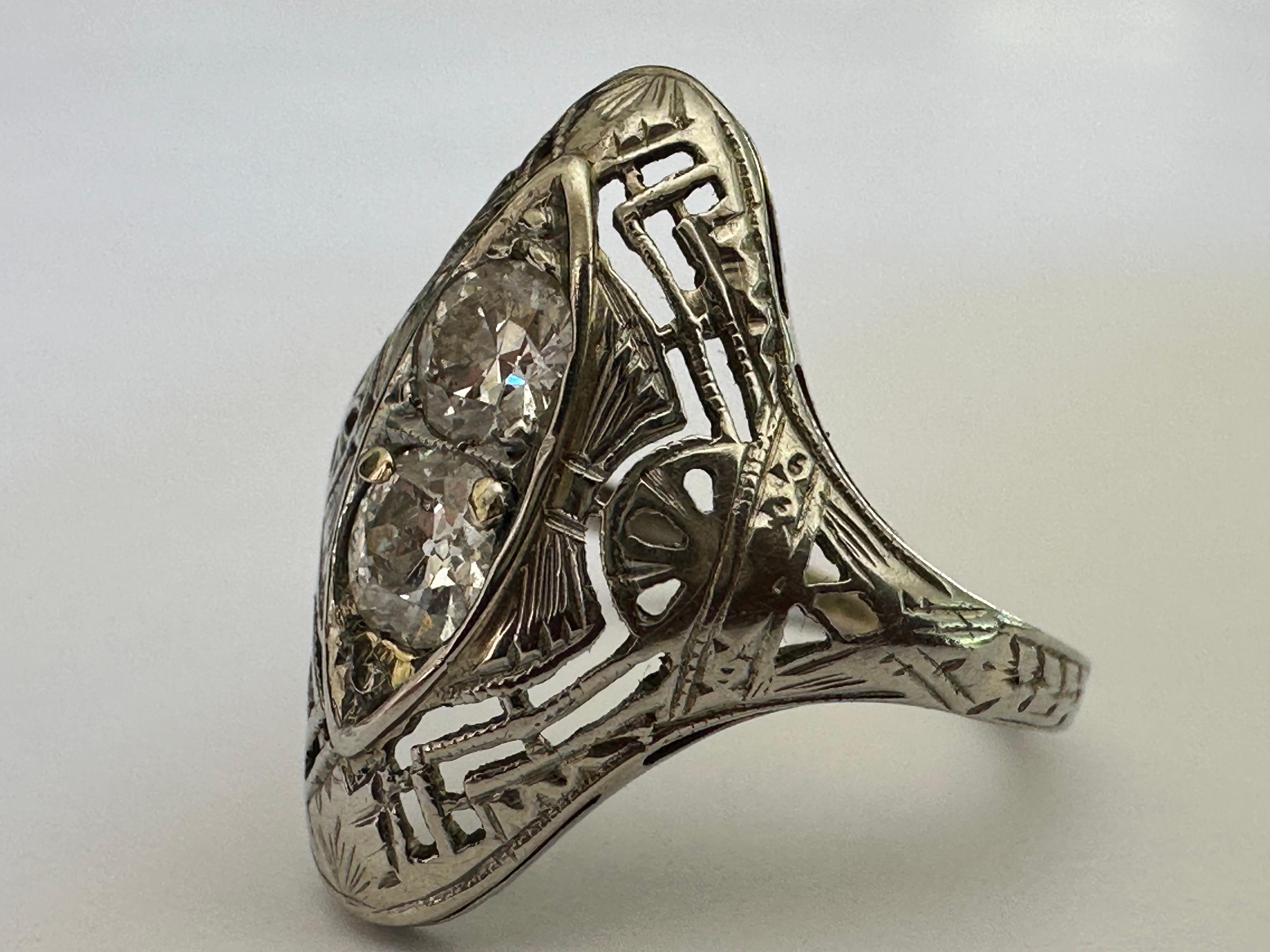 Two Old European-cut diamonds together weighing approximately 0.55 carat shine from within a navette-shaped frame accented with fanciful filigree in this classic Art Deco dinner ring. Set in 18K white gold. 
