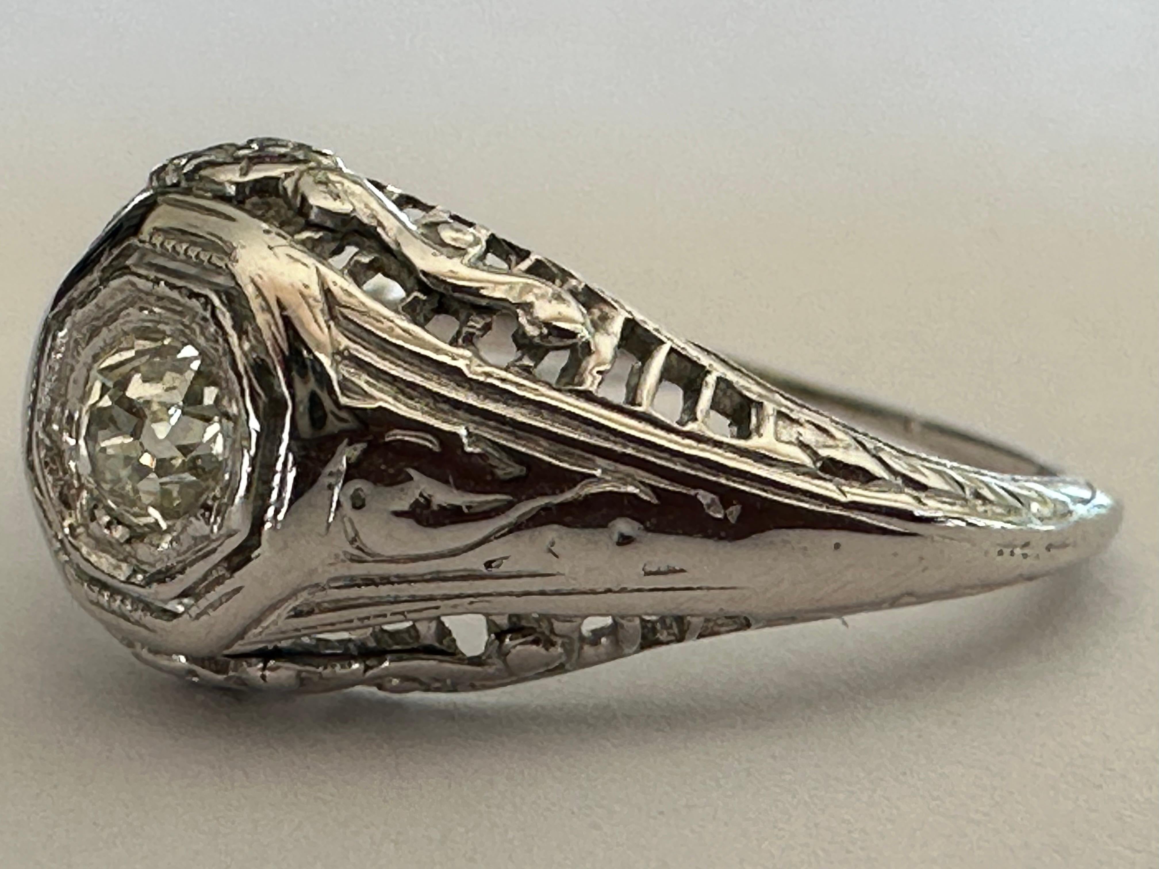 This striking band is crafted from 18k white gold with fine filigree details and set with an Old Mine cut diamond center stone measuring approximately 0.18 carats, IJ color, VS clarity. Circa 1920s. 