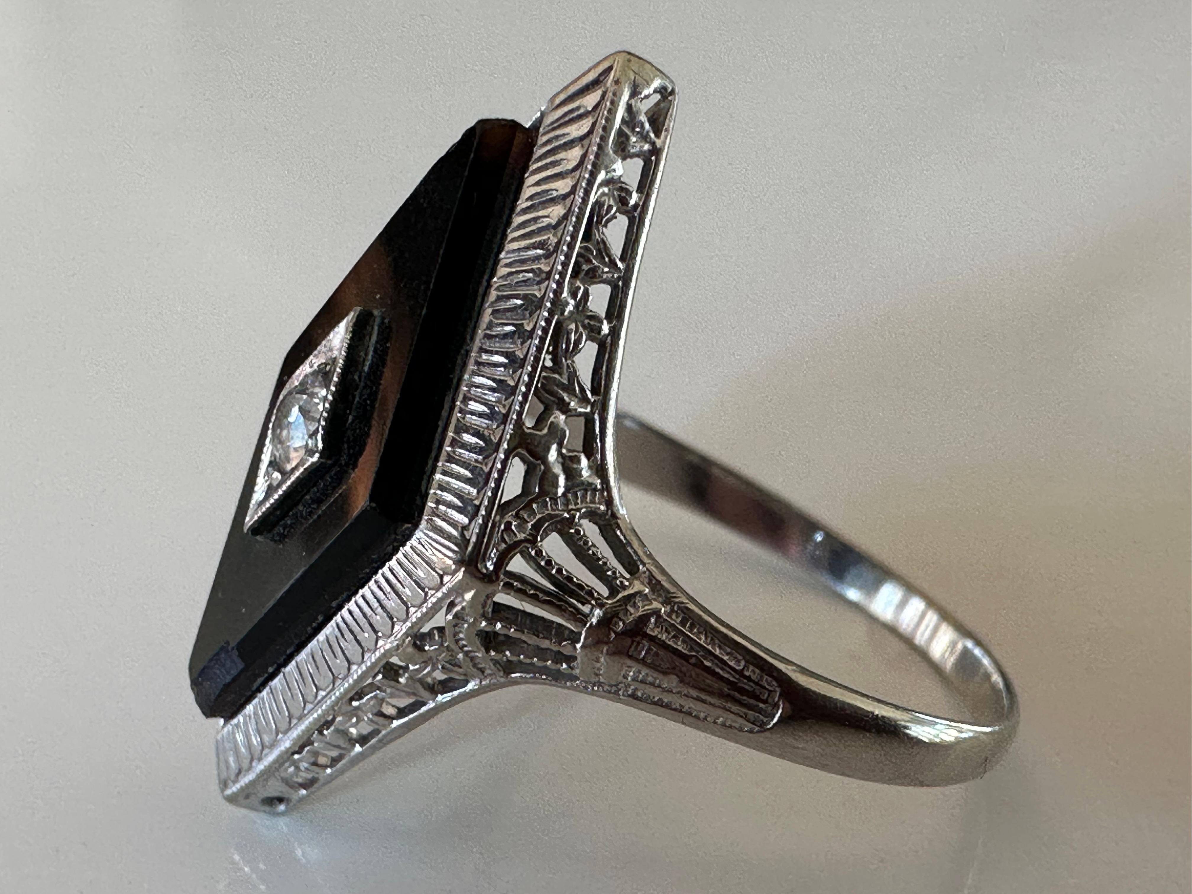 This striking Art Deco navette-shaped dinner ring is composed of black onyx, center-pierced with a single sparkling Old European-cut diamond measuring 0.10 carats, F color, VS clarity, and complemented with fine filigree handcrafted in 18K white