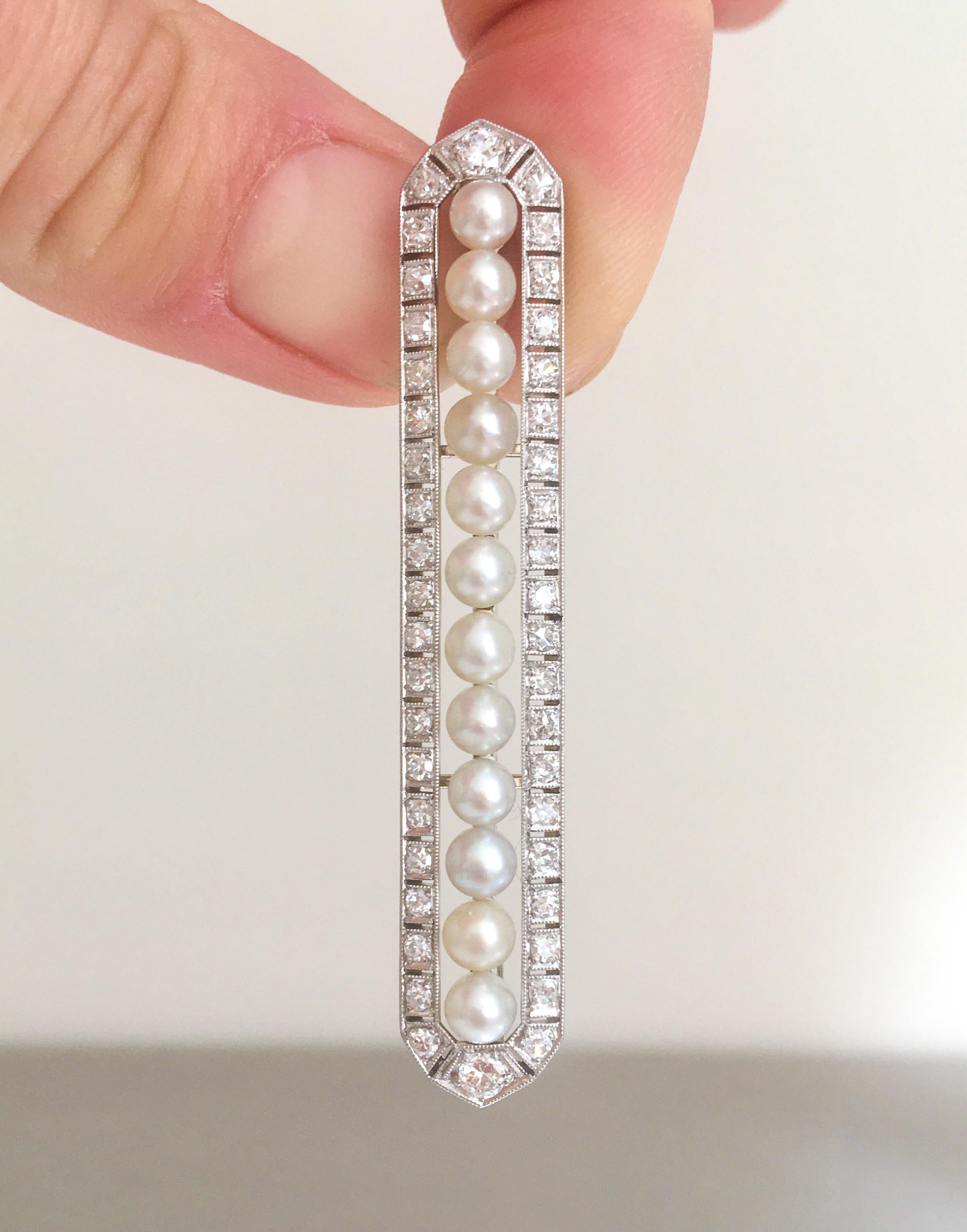 This gorgeous 1930's Art Deco diamond and pearl bar brooch is set in an 18 karat gold platinum frame. The brooch is embellished with twelve clear round cultured pearls, surrounded by a halo of shimmering old cut diamonds, displayed within mille