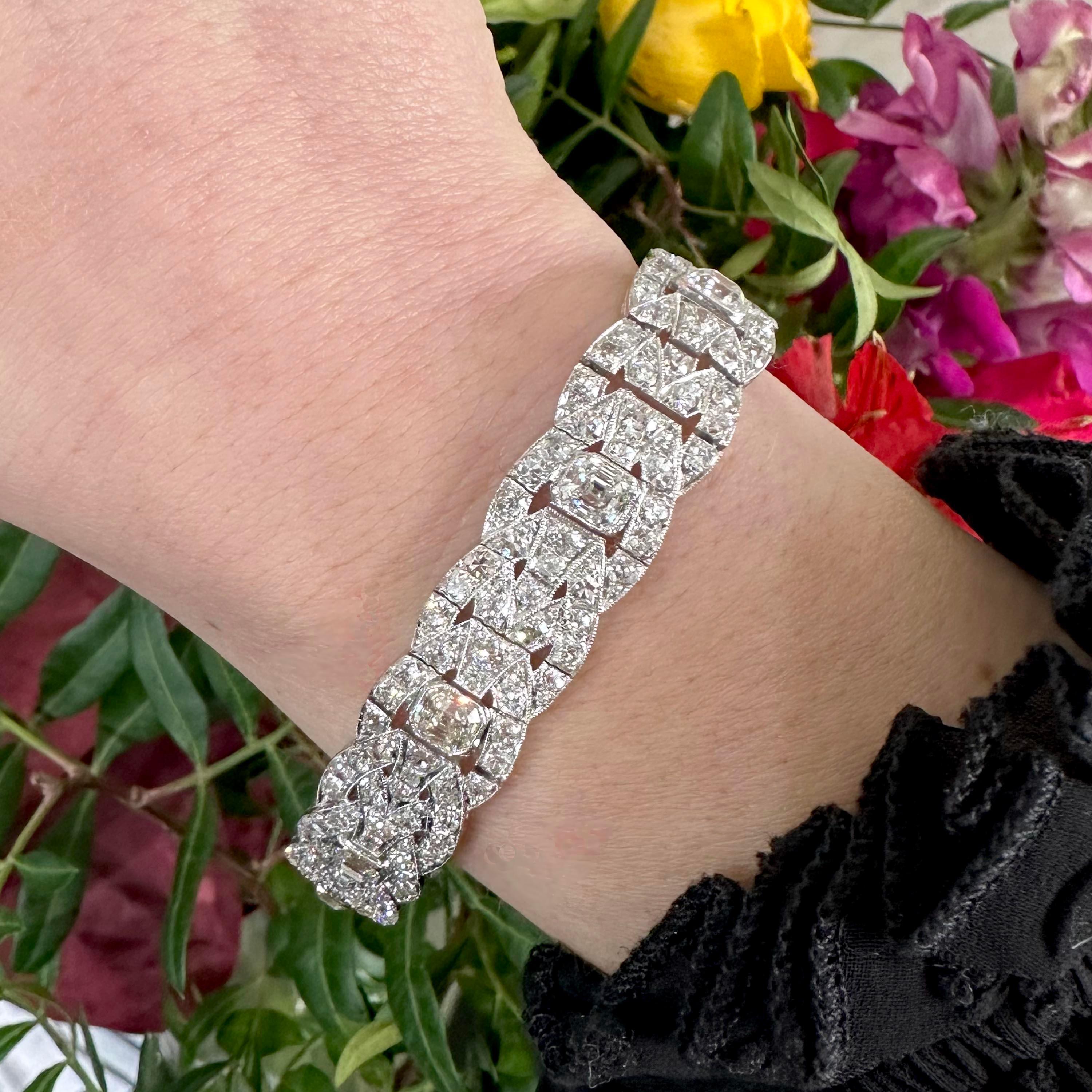 An Art Deco diamond bracelet, set with nine, emerald-cut diamonds, in rub over settings, in a repeat design of old-cut and eight-cut diamond set interlocking oval loops, tapering to Y shapes, with millegrain edged decoration, with scroll engraved
