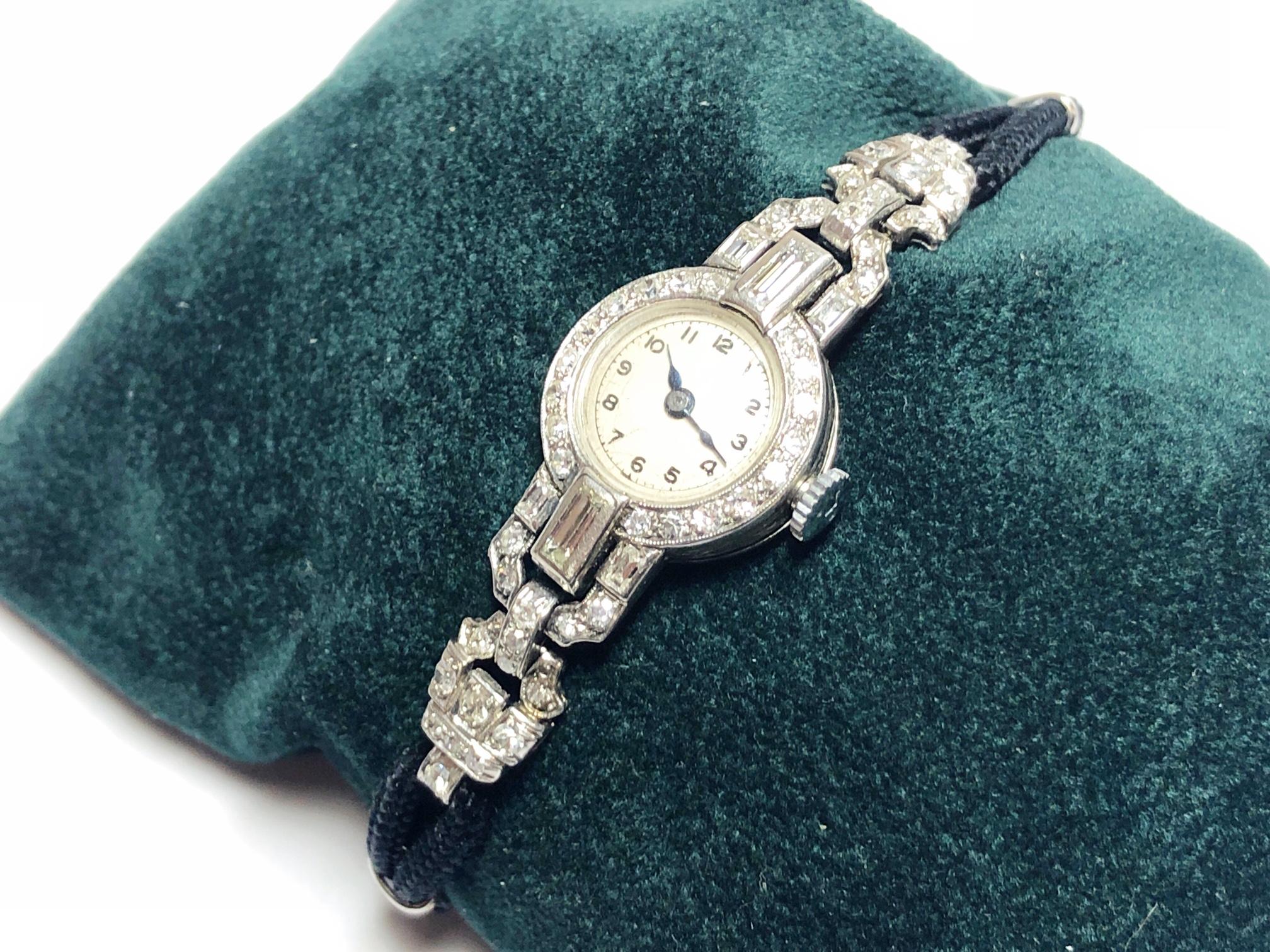 Eine Art-Deco-Cocktail-Armbanduhr mit Diamanten und Platin, mit weißem, rundem Zifferblatt, mit schwarzen arabischen handgemalten Ziffern, innerhalb eines Ringes von Minutenziffern, mit blauen Stahlzeigern, mit einer Einfassung aus Diamanten im