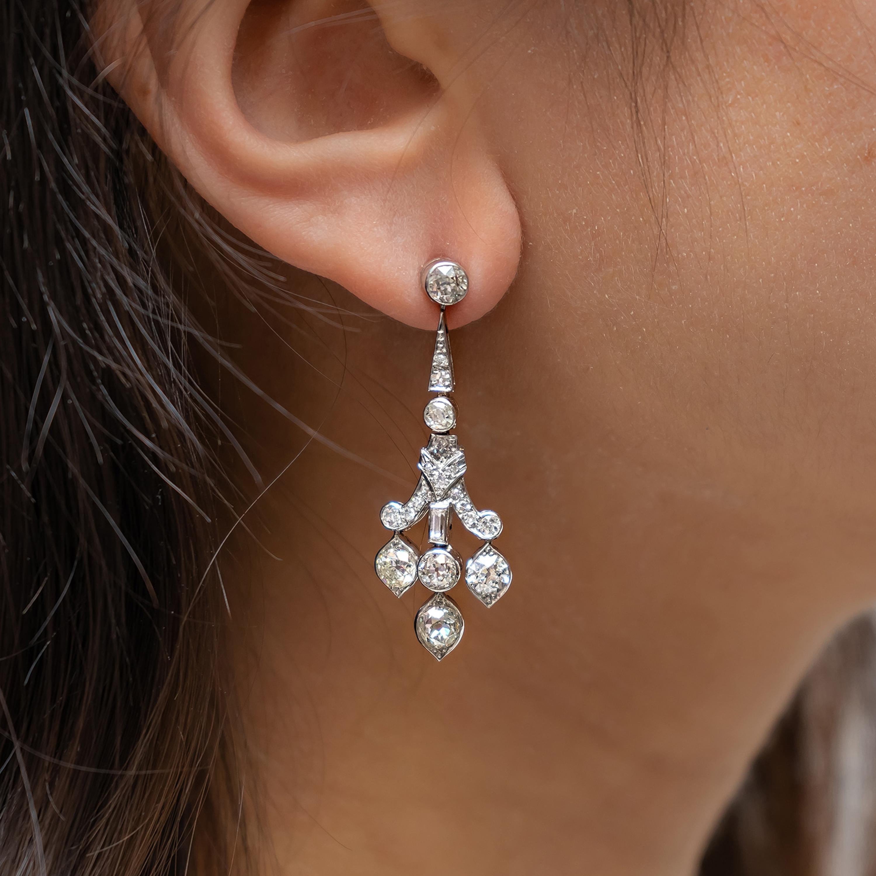 Paire de boucles d'oreilles Art déco en diamant, avec un motif géométrique et en volutes, articulé, avec des diamants baguettes et des diamants taille ancienne, dans des montures en frottement et en grain, avec trois diamants taille ancienne